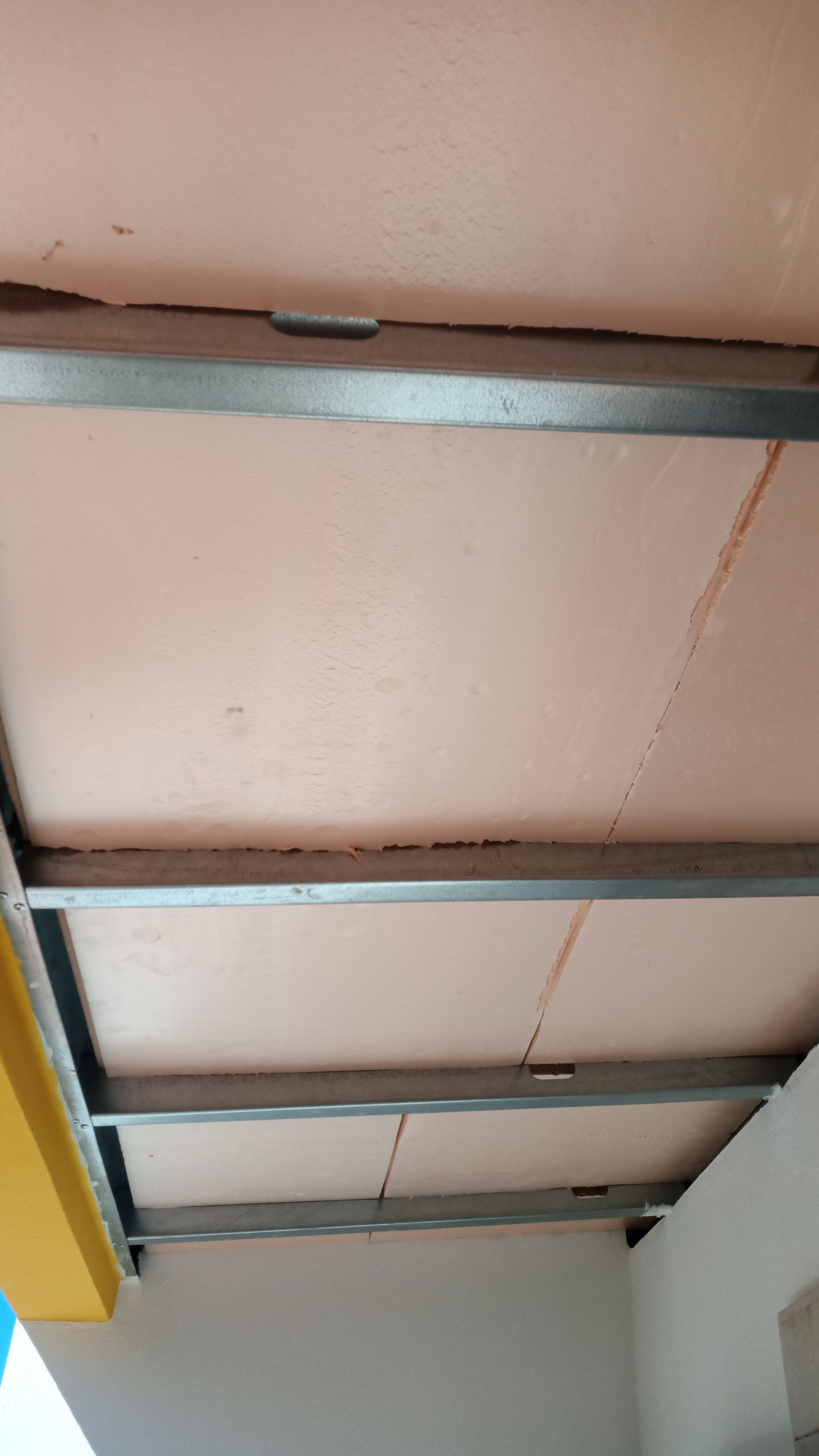 Teto com estrutura metálica e placas de isolamento em tom rosa-bege.