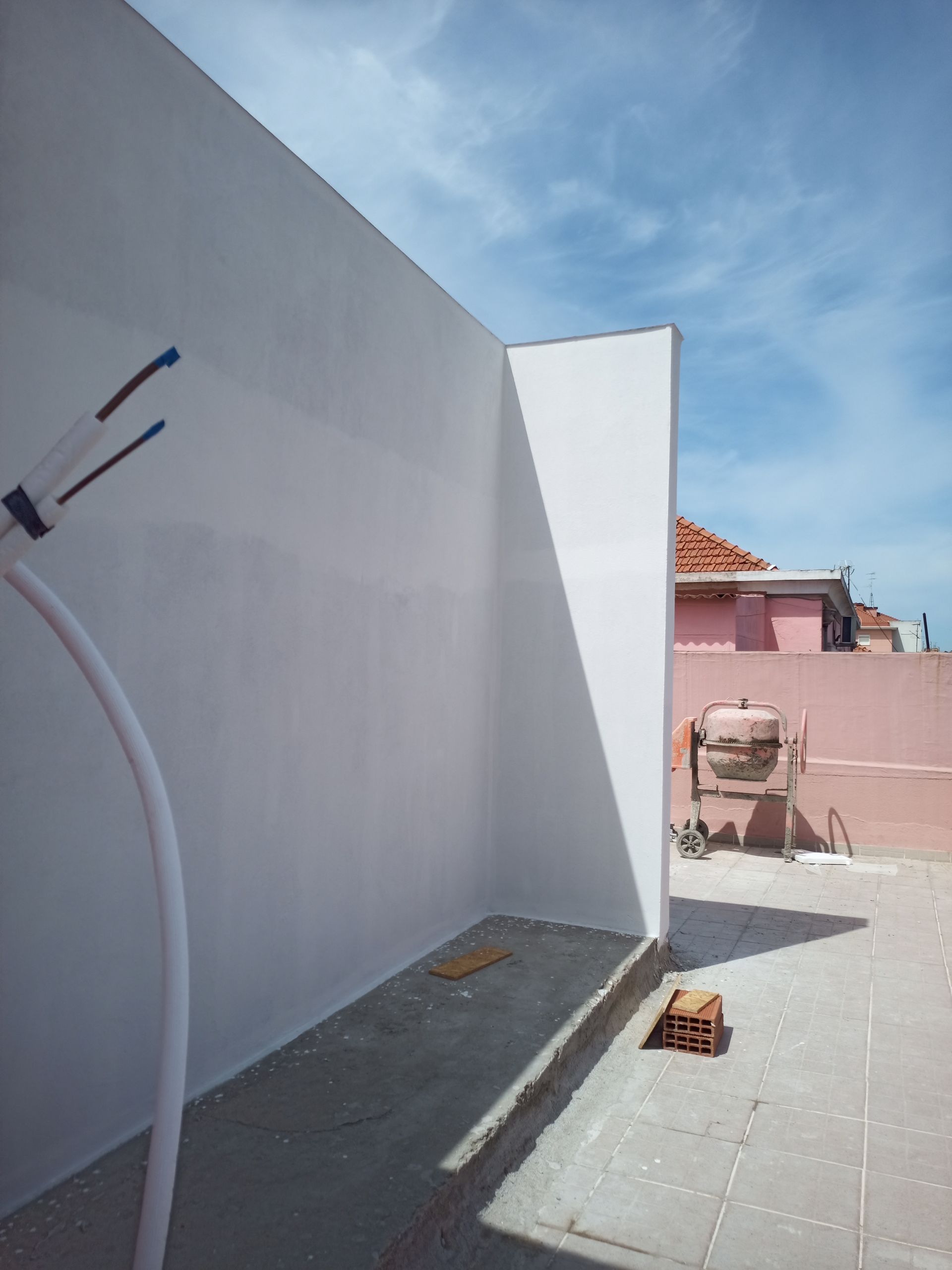 Paredes pintadas de branco em um terraço com um céu azul ensolarado ao fundo.
