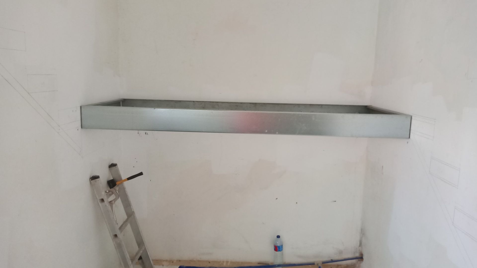 Uma prateleira de metal está fixada em uma parede branca. Uma escada está encostada na parede abaixo.