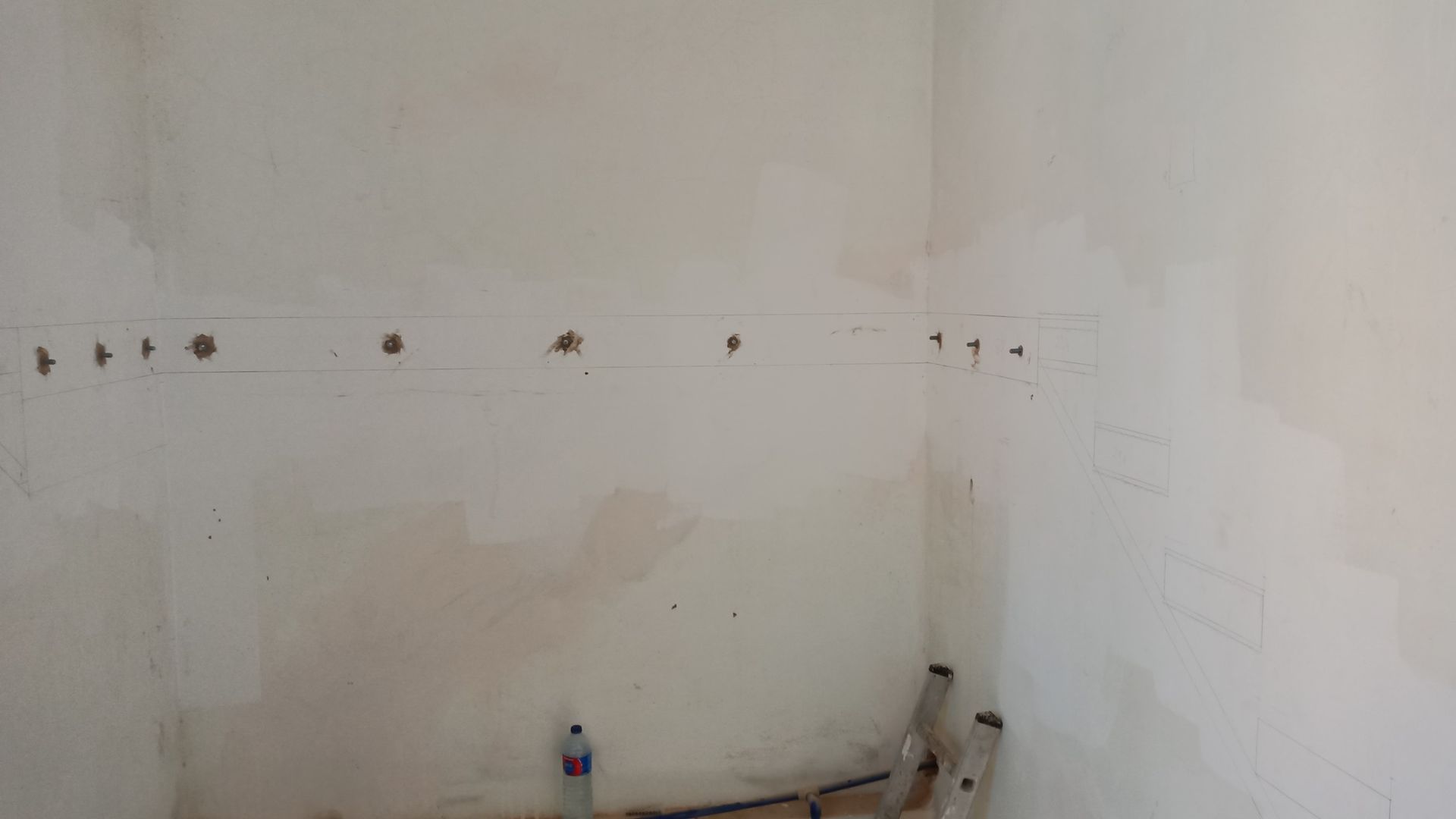 Vista interna de um cômodo com paredes inacabadas. Vários furos foram feitos na parede e canos são visíveis na parte inferior.