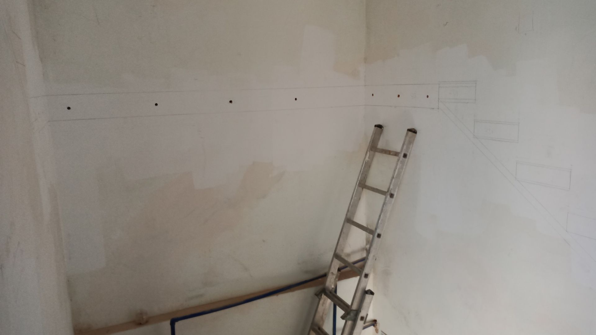Escada encostada em uma parede branca com marcas e buracos, em um cômodo em construção.