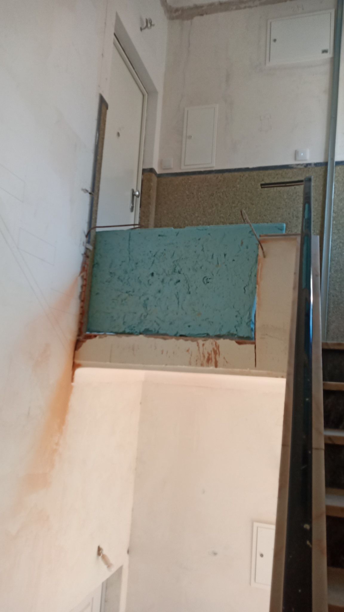 Escadaria com tinta descascando, mostrando os degraus, uma porta e seções da parede com materiais variados.