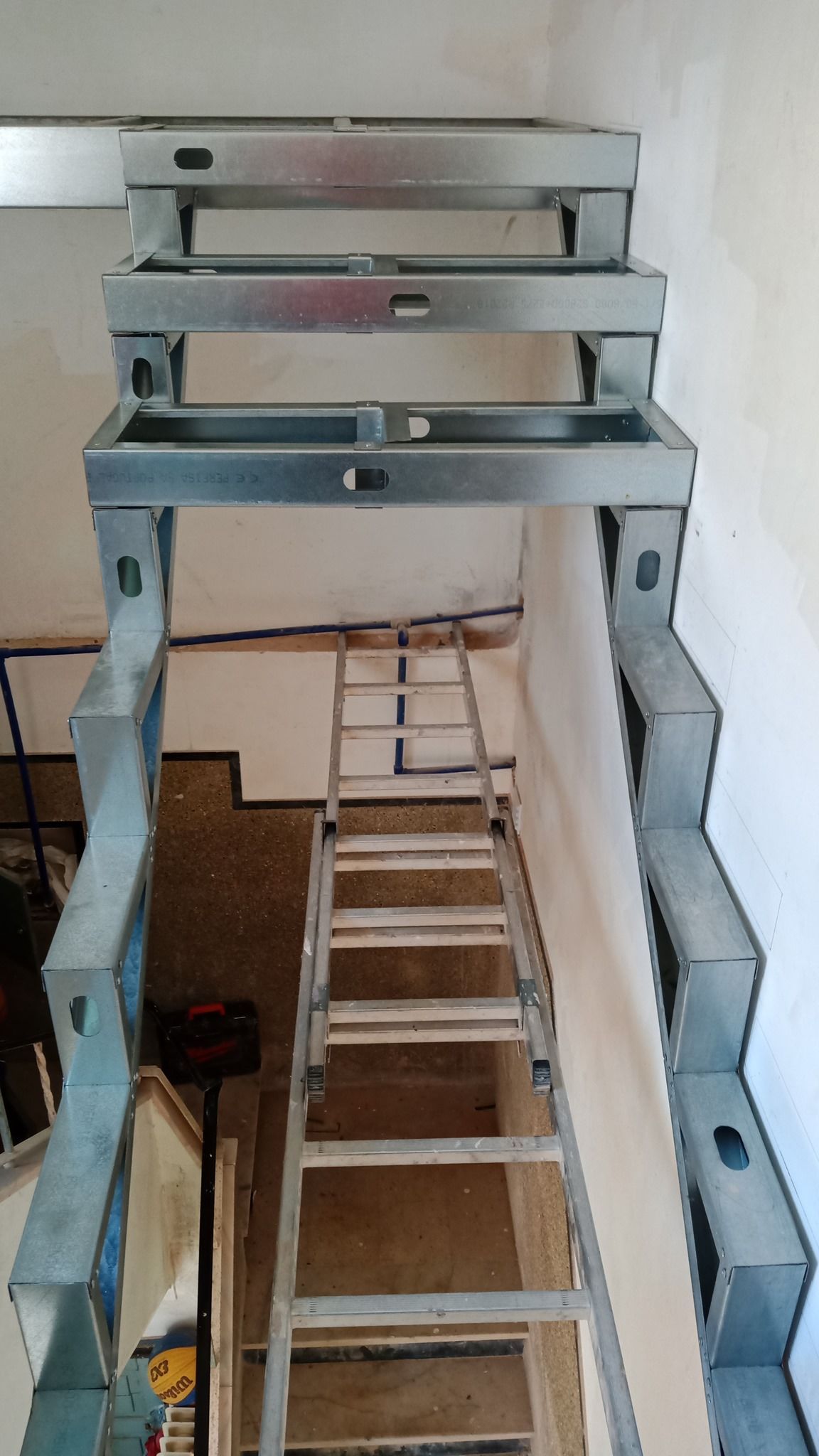 Estrutura metálica de escada em construção com uma escada de mão no meio.