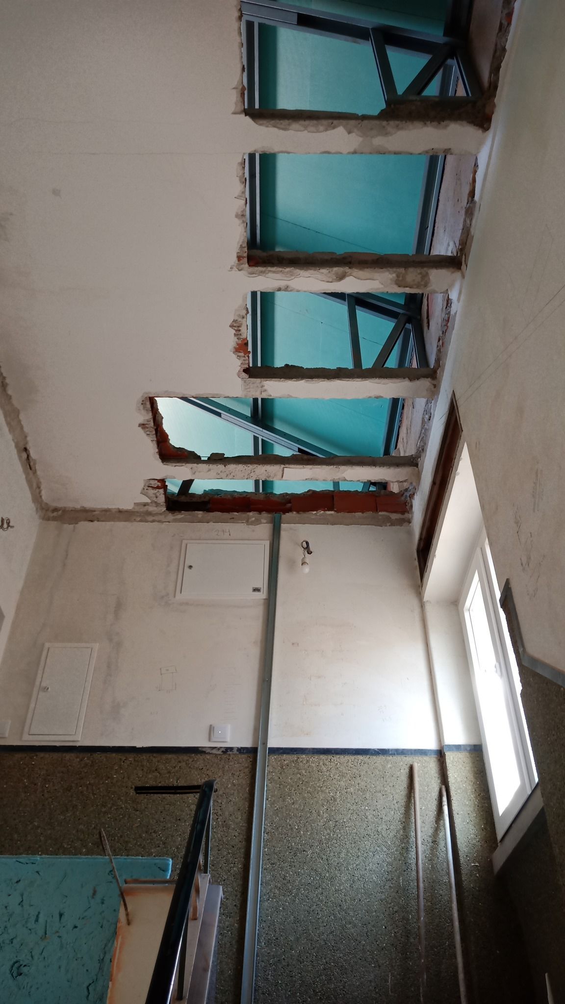 Vista interior mostrando a demolição do teto com aberturas que revelam um céu azul e vigas de sustentação.