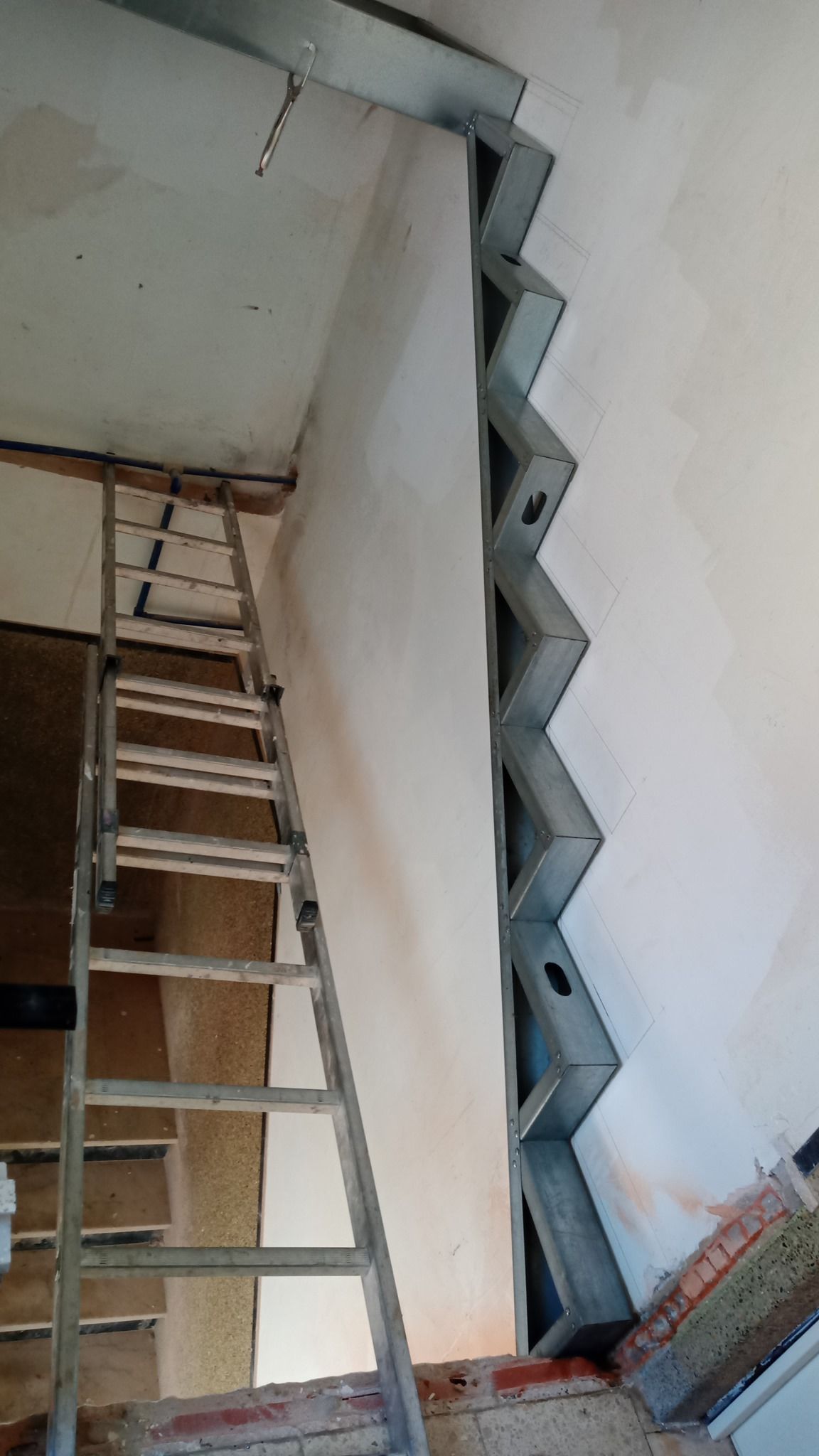 Longarina metálica de escada instalada em uma parede com uma escada encostada nela. Construção em andamento.