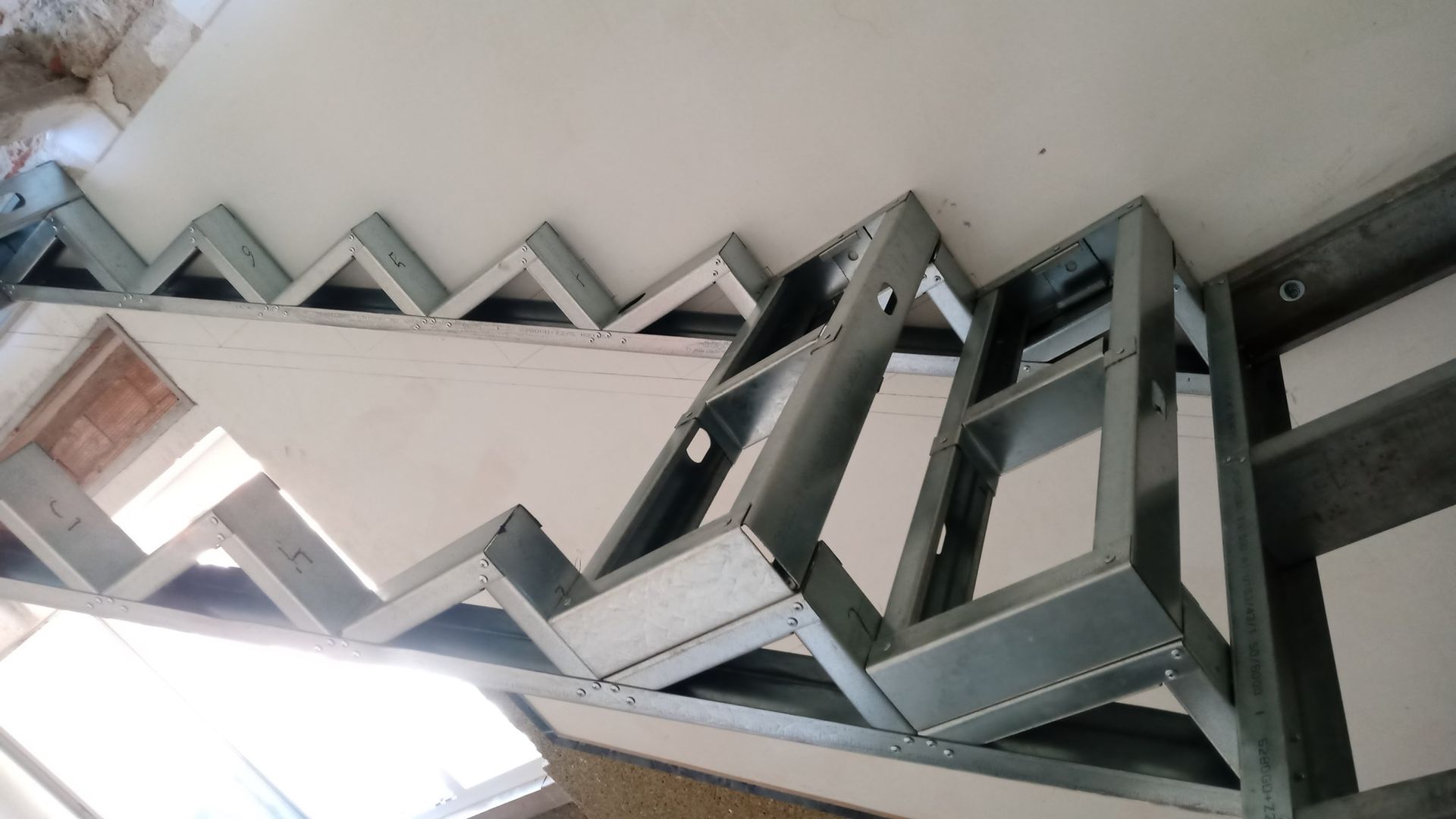 Estrutura metálica para um teto em ziguezague, parcialmente revestida com drywall em um cômodo.