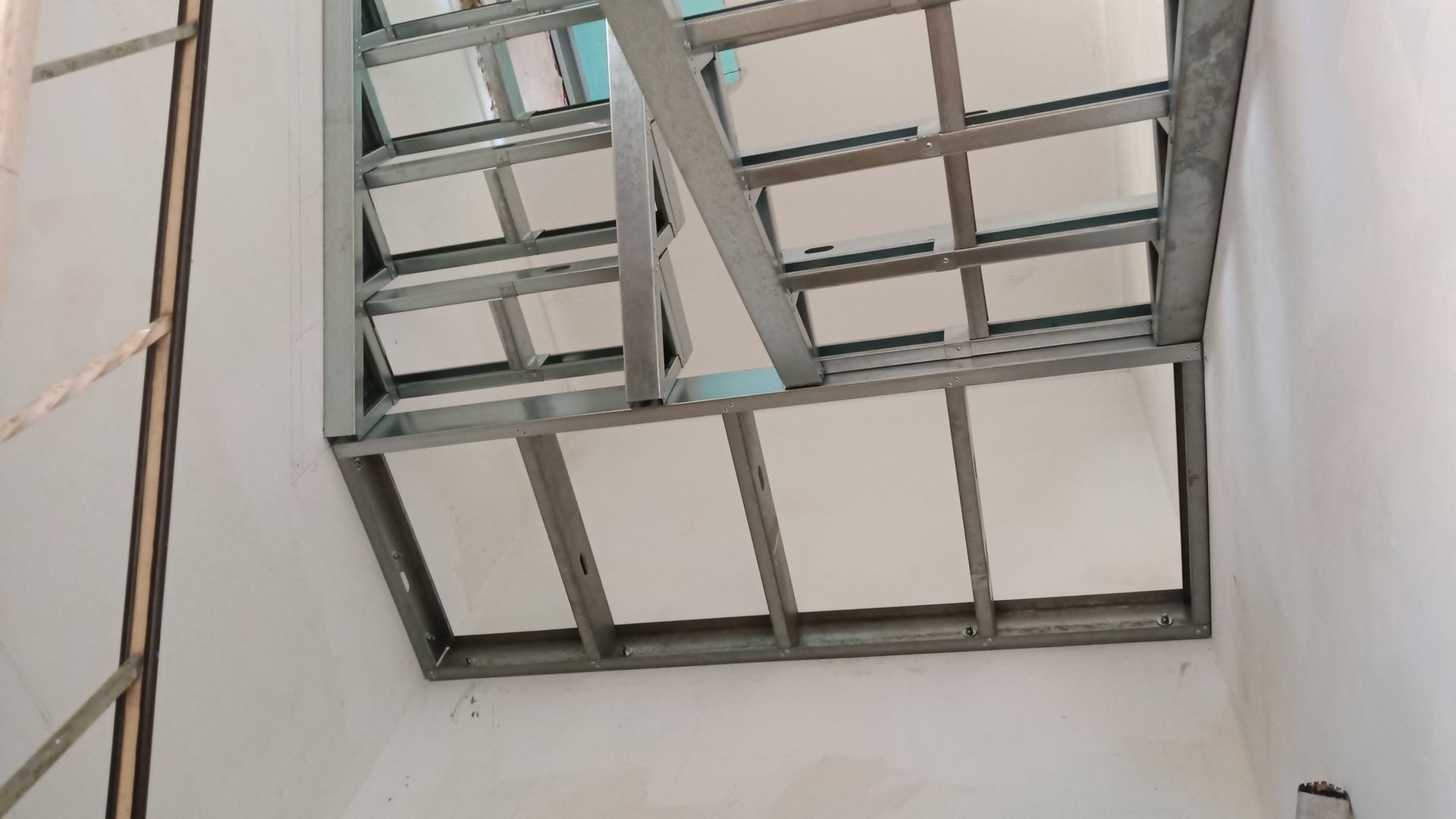 Estrutura metálica e painéis brancos formando um teto ou a parte superior da parede em uma sala com paredes brancas.