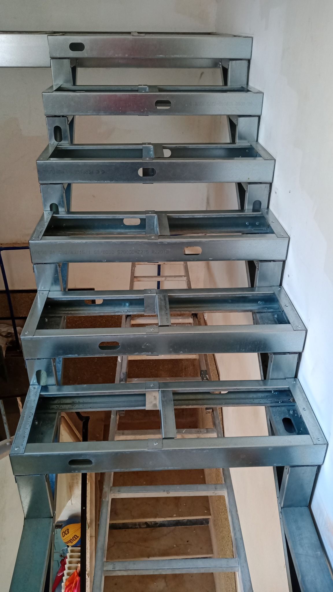 Estrutura metálica da escada, construção aberta, contra uma parede branca.