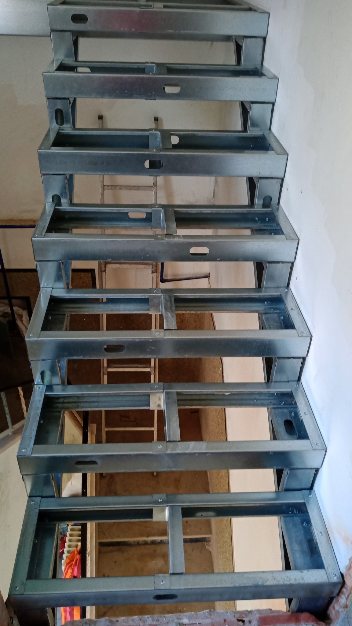 Estrutura metálica de escada, vista de cima, construída em um edifício. Degraus horizontais e suportes verticais são visíveis.