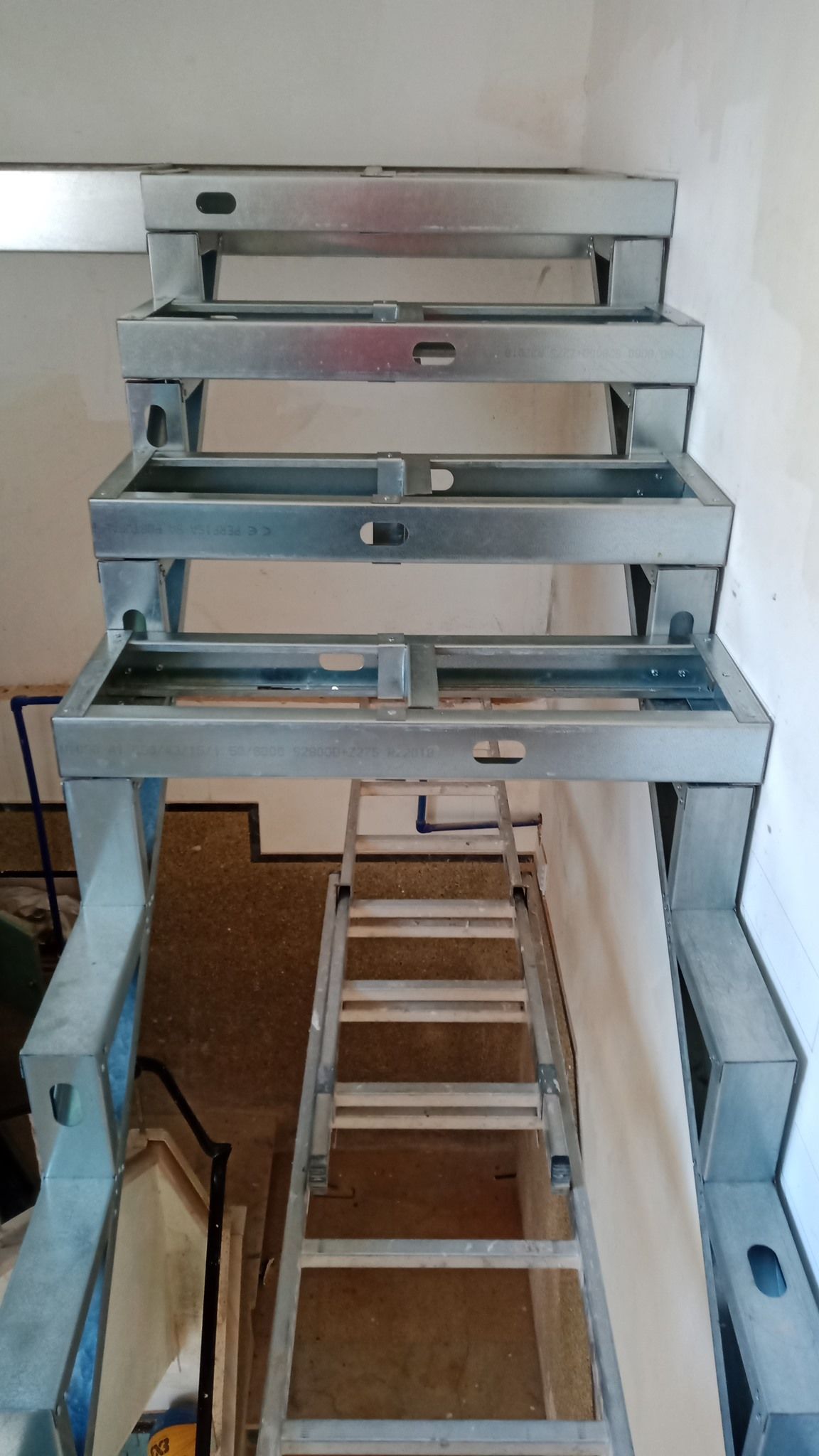 Estrutura metálica de escada em construção, com uma escada encostada nela.