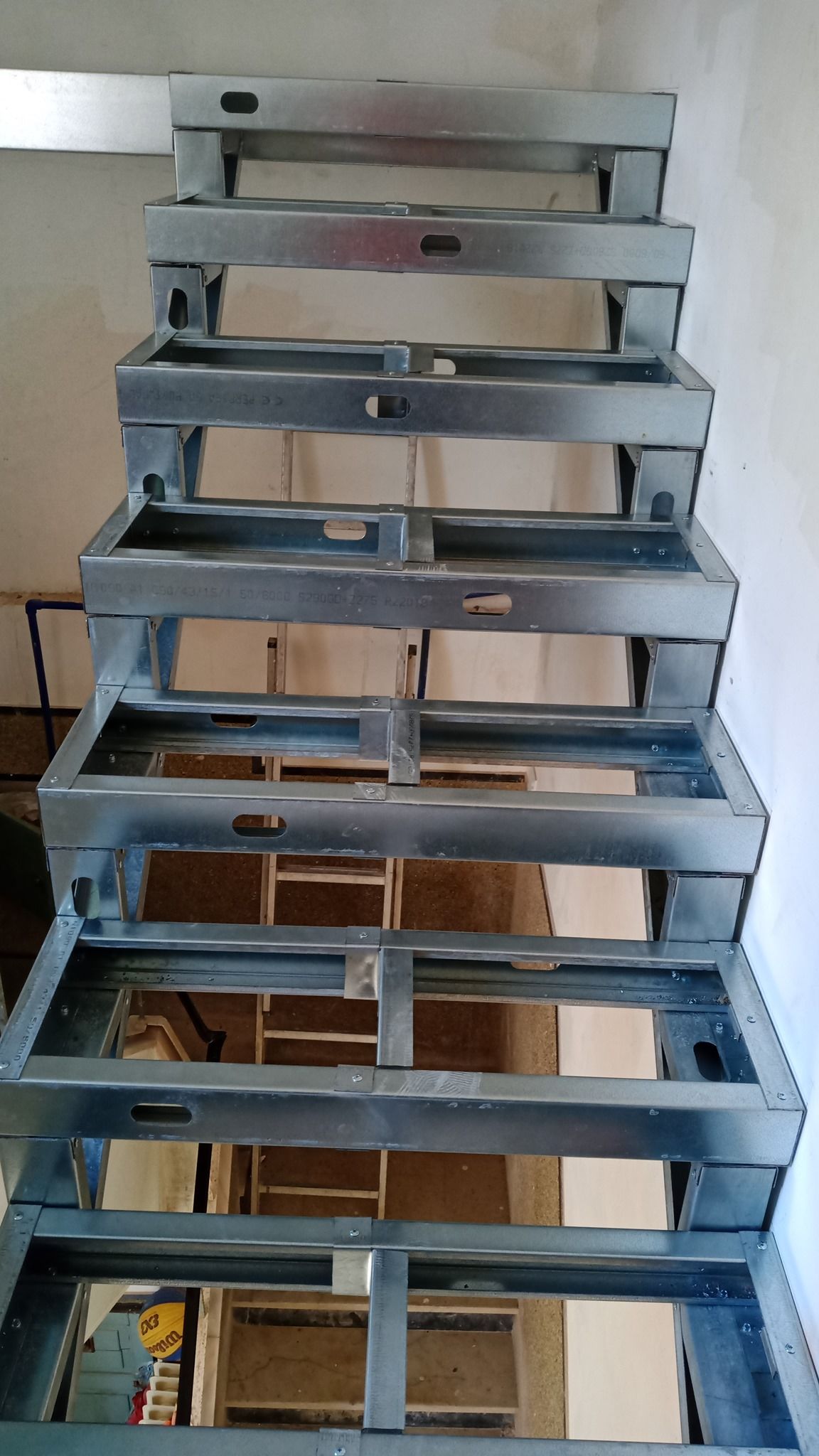 Estrutura metálica da escada, vista por baixo, com degraus retangulares abertos, pronta para instalação.