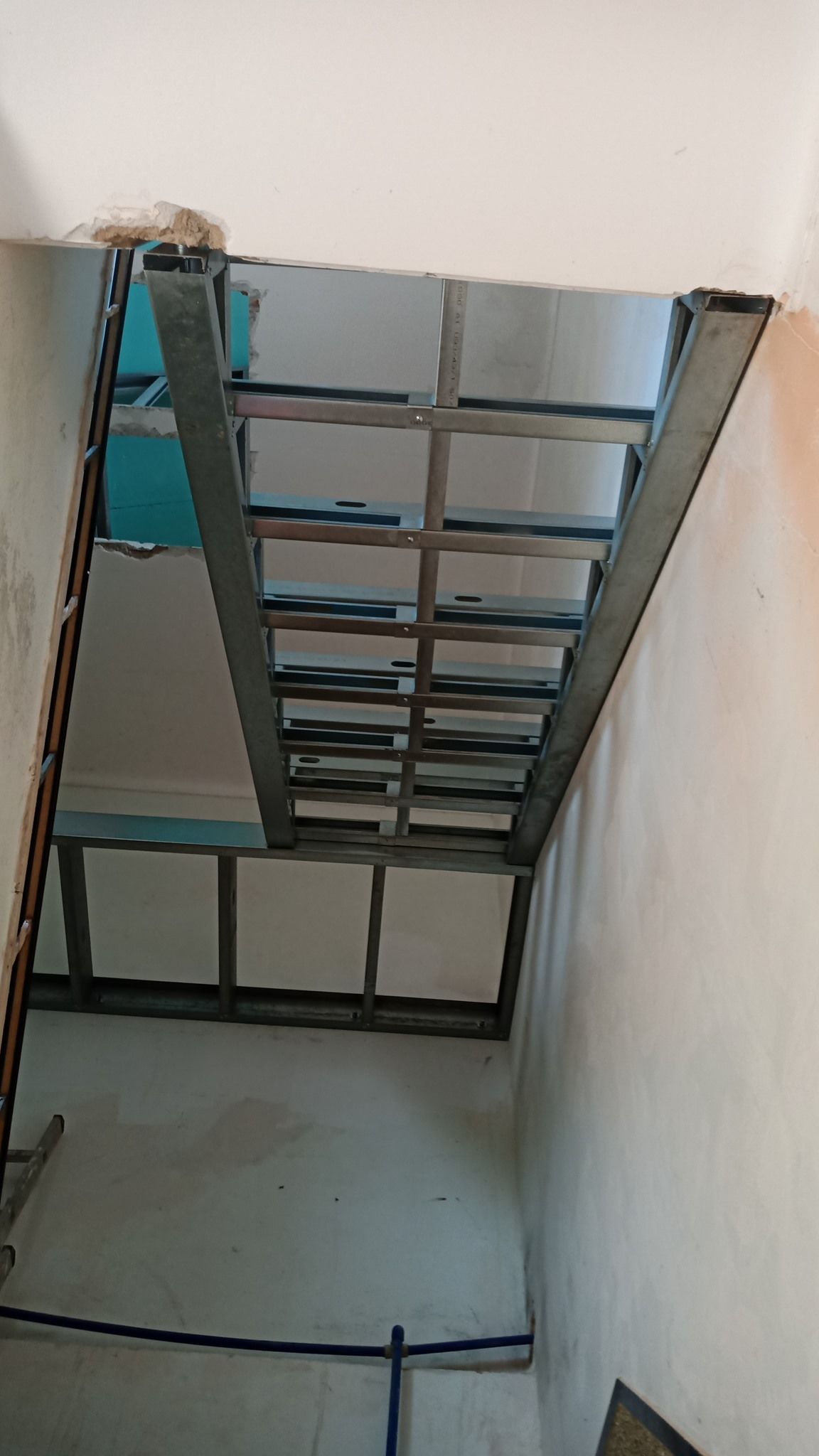 Estrutura de teto com armação metálica, parcialmente revestida com isolamento azul e painéis brancos, dentro de uma sala.