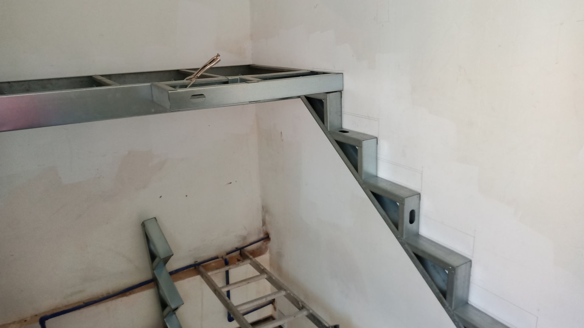 Escada com estrutura metálica que leva a uma plataforma construída em uma sala com paredes brancas.