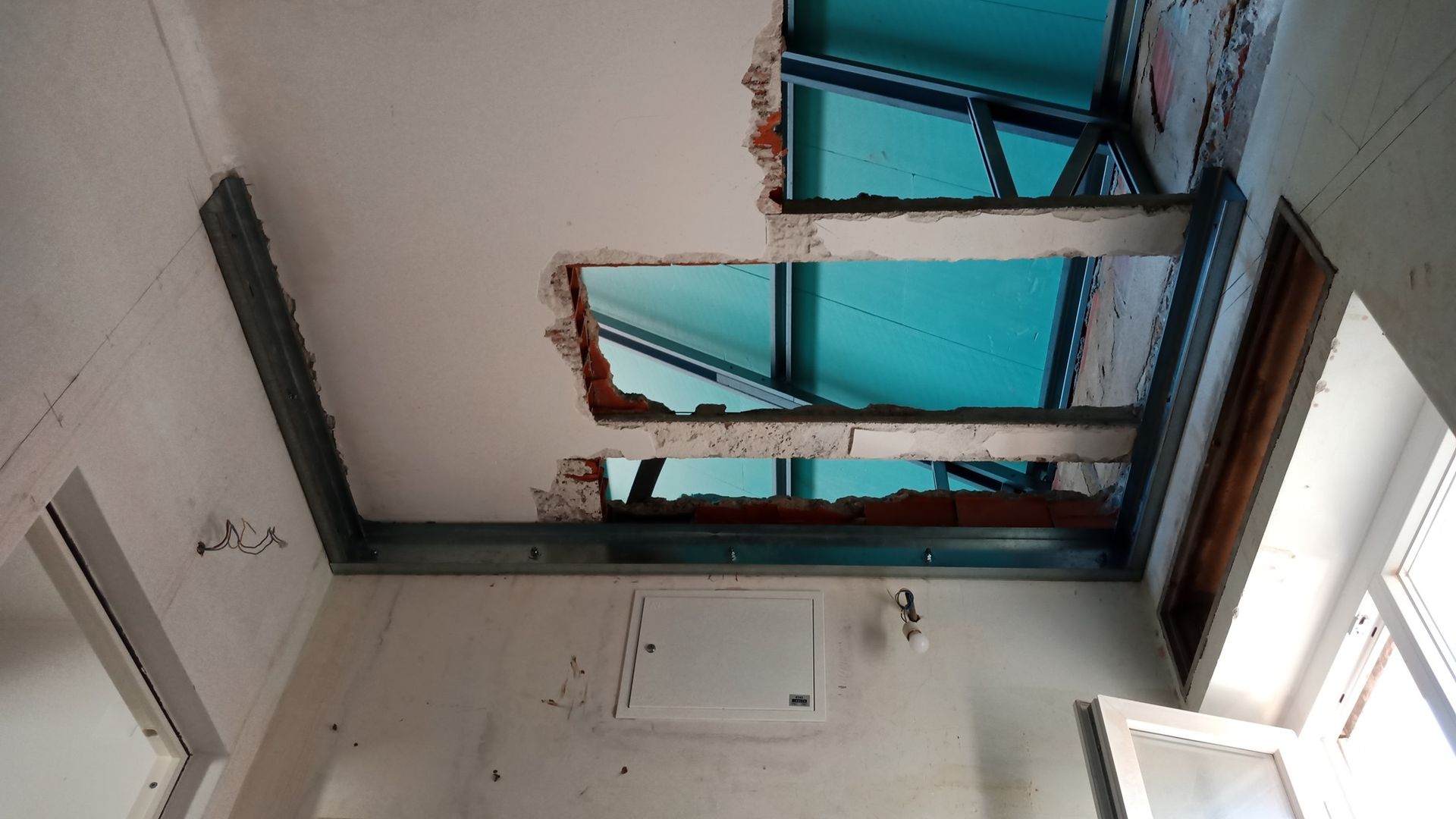 Teto danificado com buracos que revelam a estrutura metálica e o céu azul, em um cômodo em reforma.