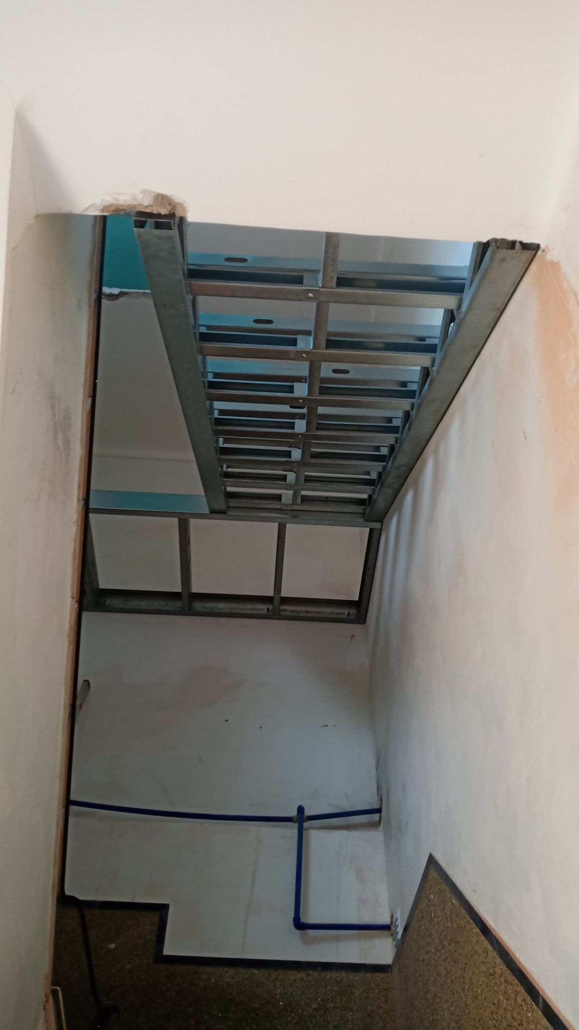 Estrutura metálica para escada sendo instalada em um corredor estreito.