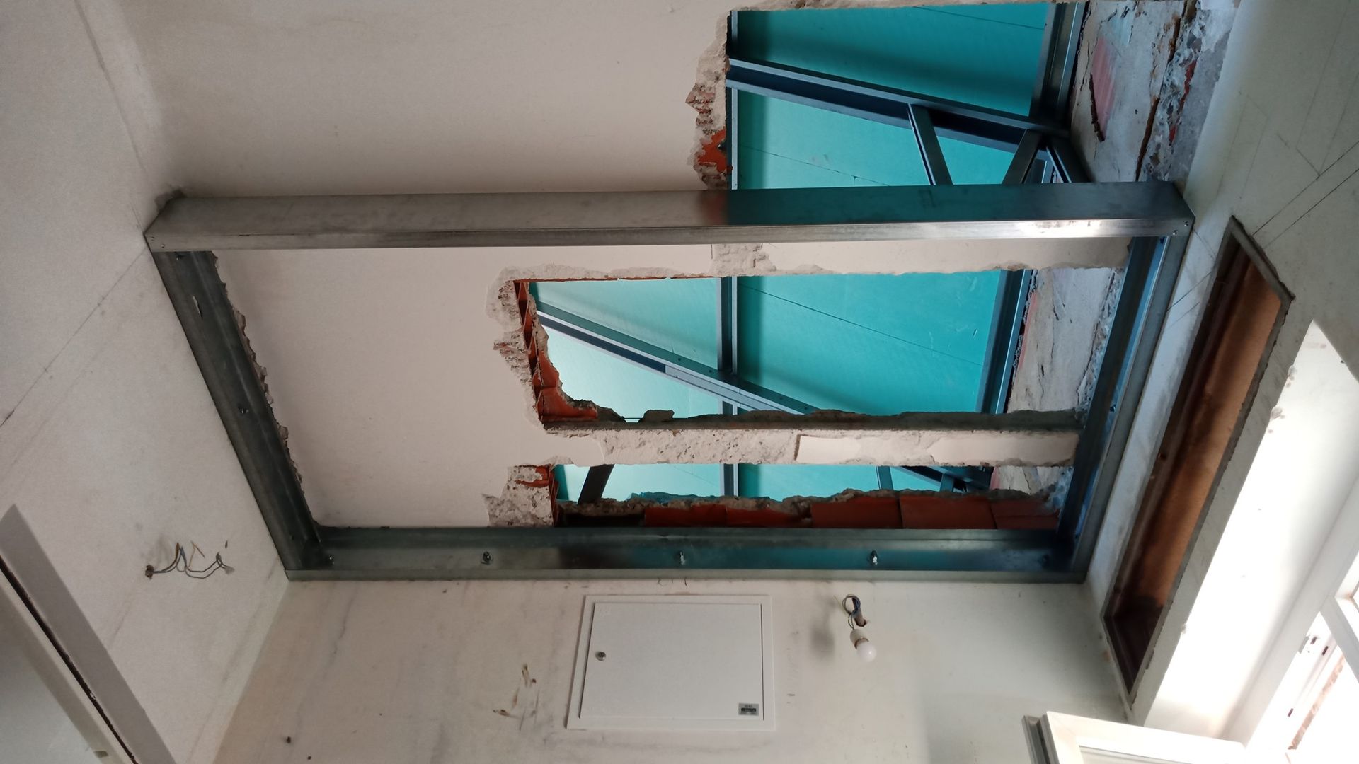 Estrutura metálica instalada no teto com um grande buraco que revela o céu. Danos nos tijolos e no gesso.