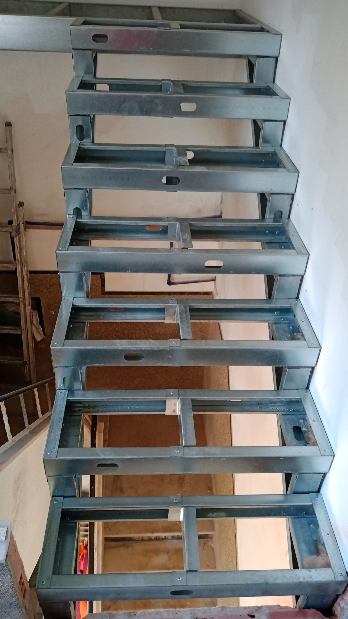 Estrutura metálica de escada em construção, montada contra uma parede branca.
