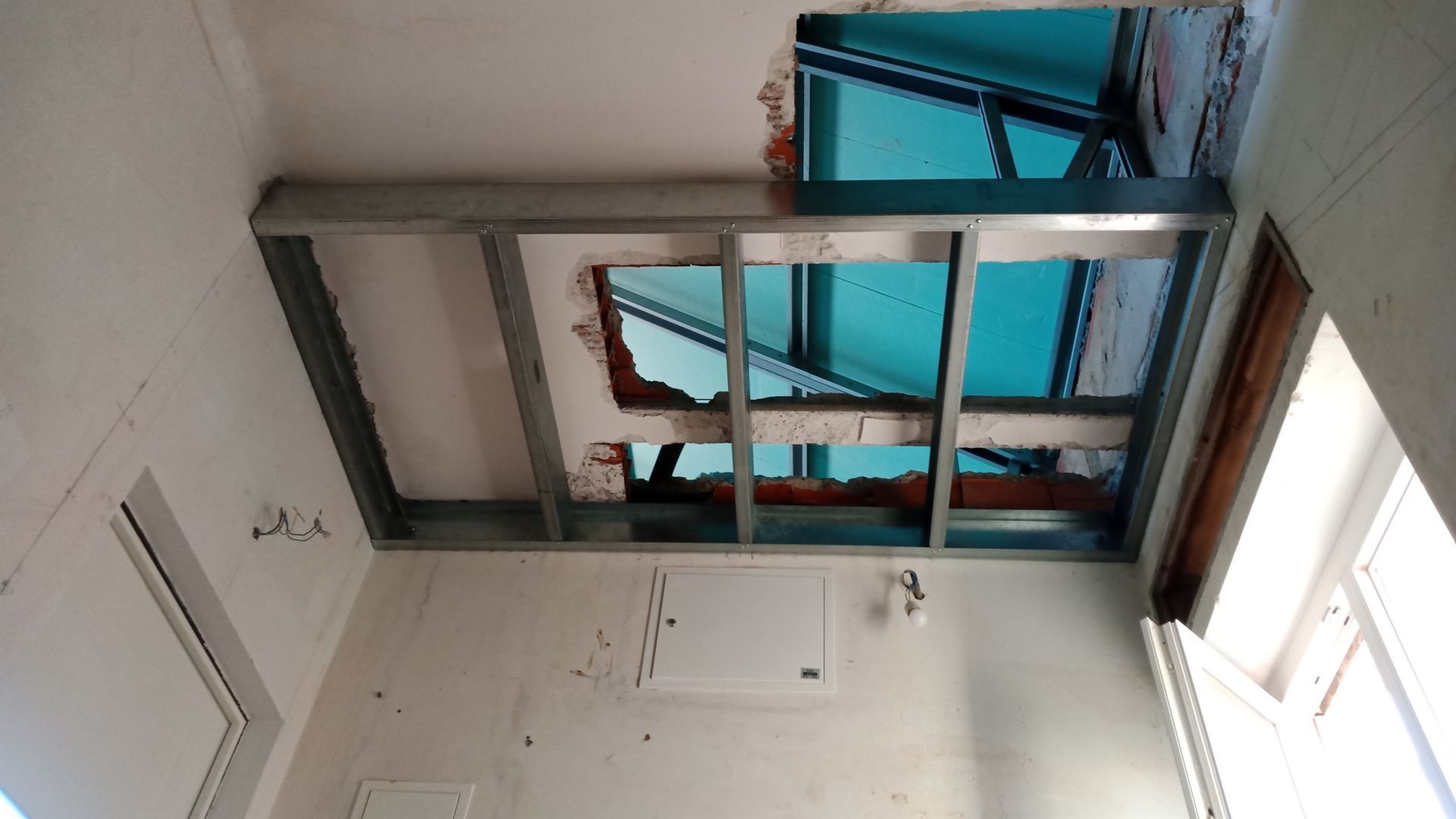 Teto danificado, telhado exposto. Estrutura metálica ao redor do buraco no teto.