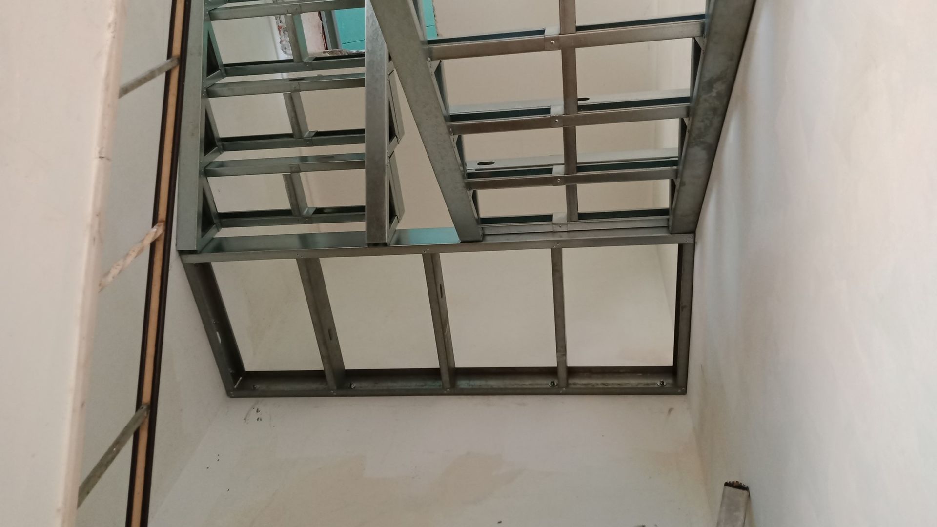 Estrutura metálica de uma escada em construção em um edifício. Paredes brancas em ambos os lados.