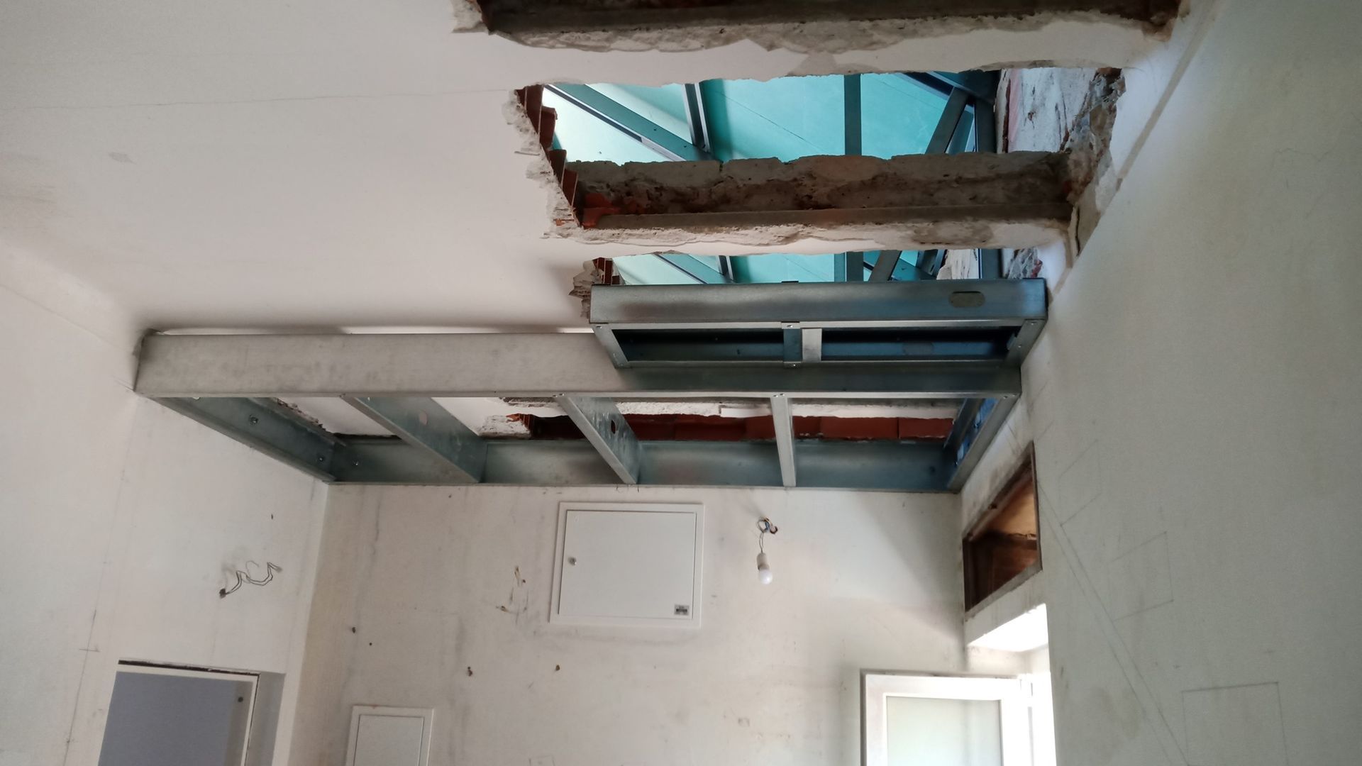 Teto com estrutura metálica exposta, dois orifícios recortados, provavelmente para sistemas de climatização ou outras instalações, em um cômodo em construção.