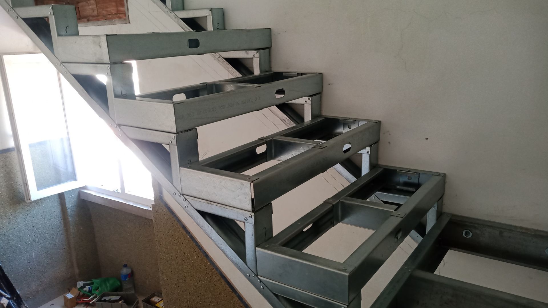 Estrutura de escada de aço sendo construída com degraus vazios, encostados em uma parede.