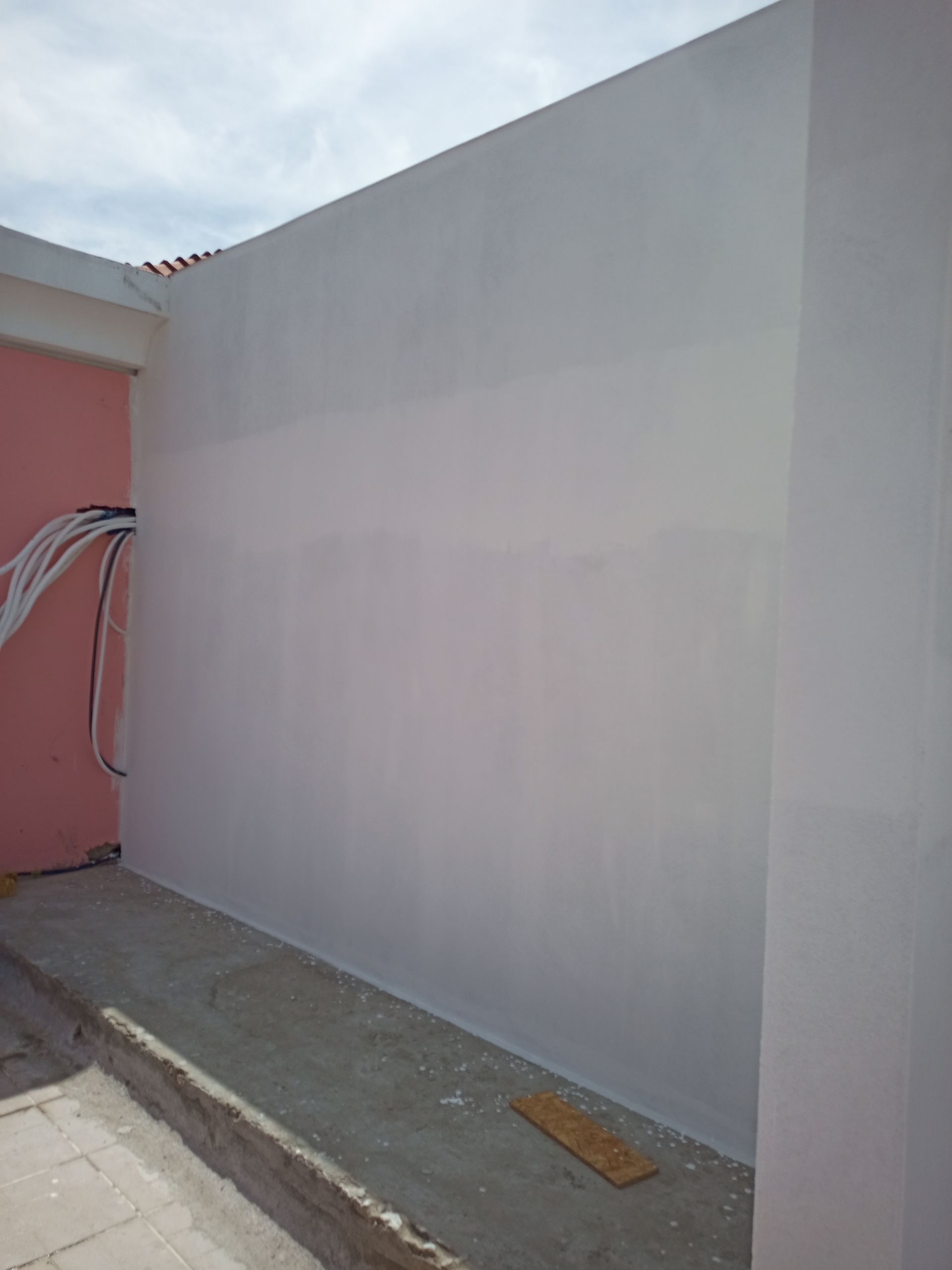 Parede externa pintada de branco com uma parede rosa à esquerda e fios expostos.