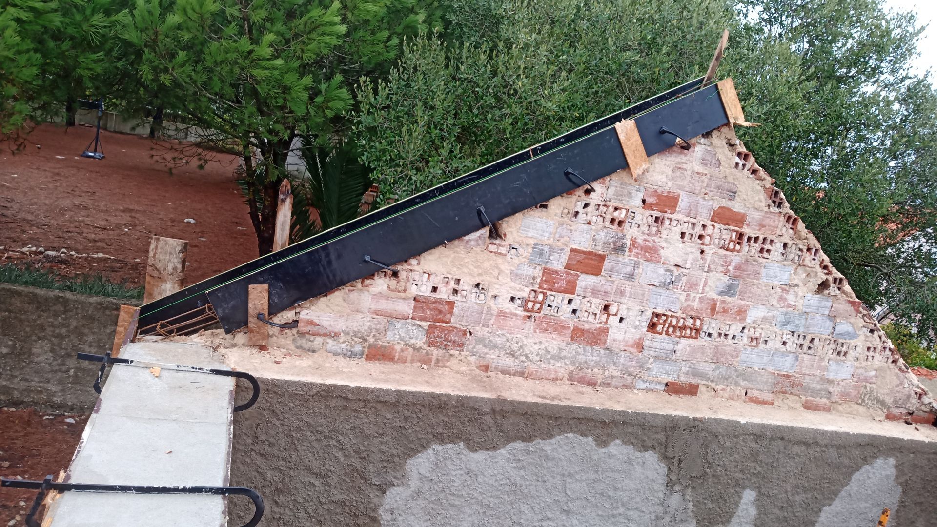 Parede de tijolos parcialmente construída com suporte de metal preto e blocos de madeira.