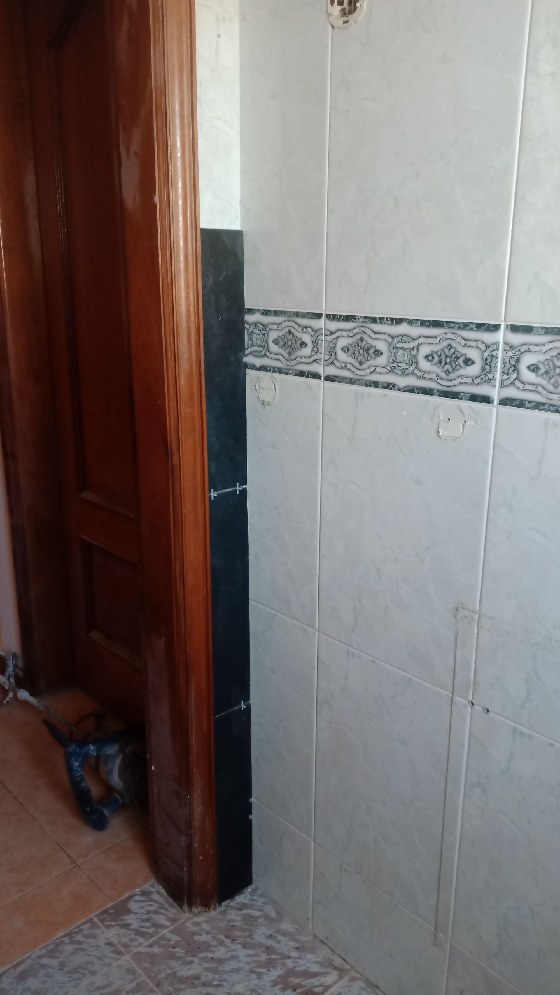 Porta de entrada com batente de madeira escura e parede revestida com azulejos brancos e pretos.