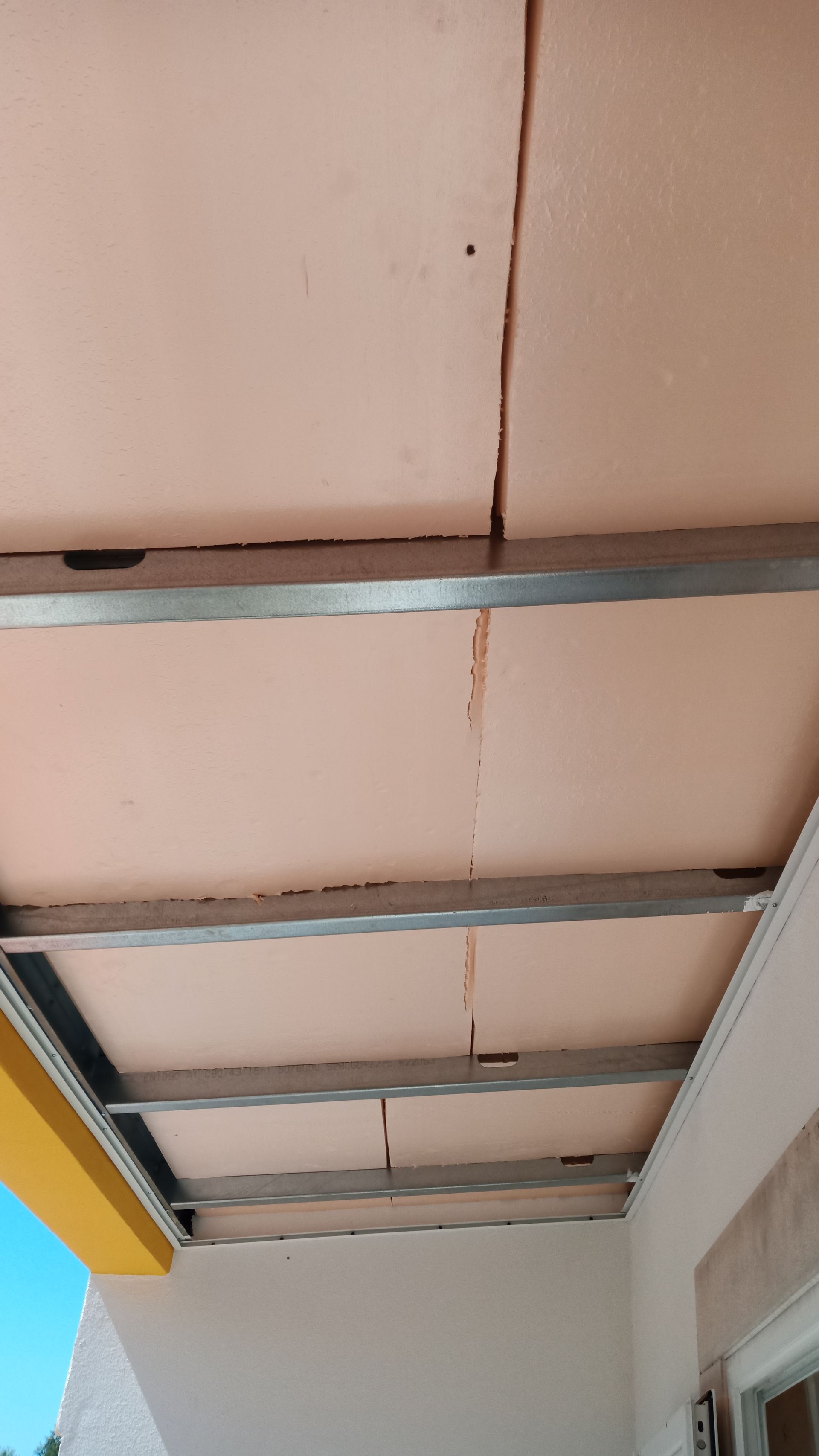 Teto rosa com rachaduras, vigas de metal visíveis.