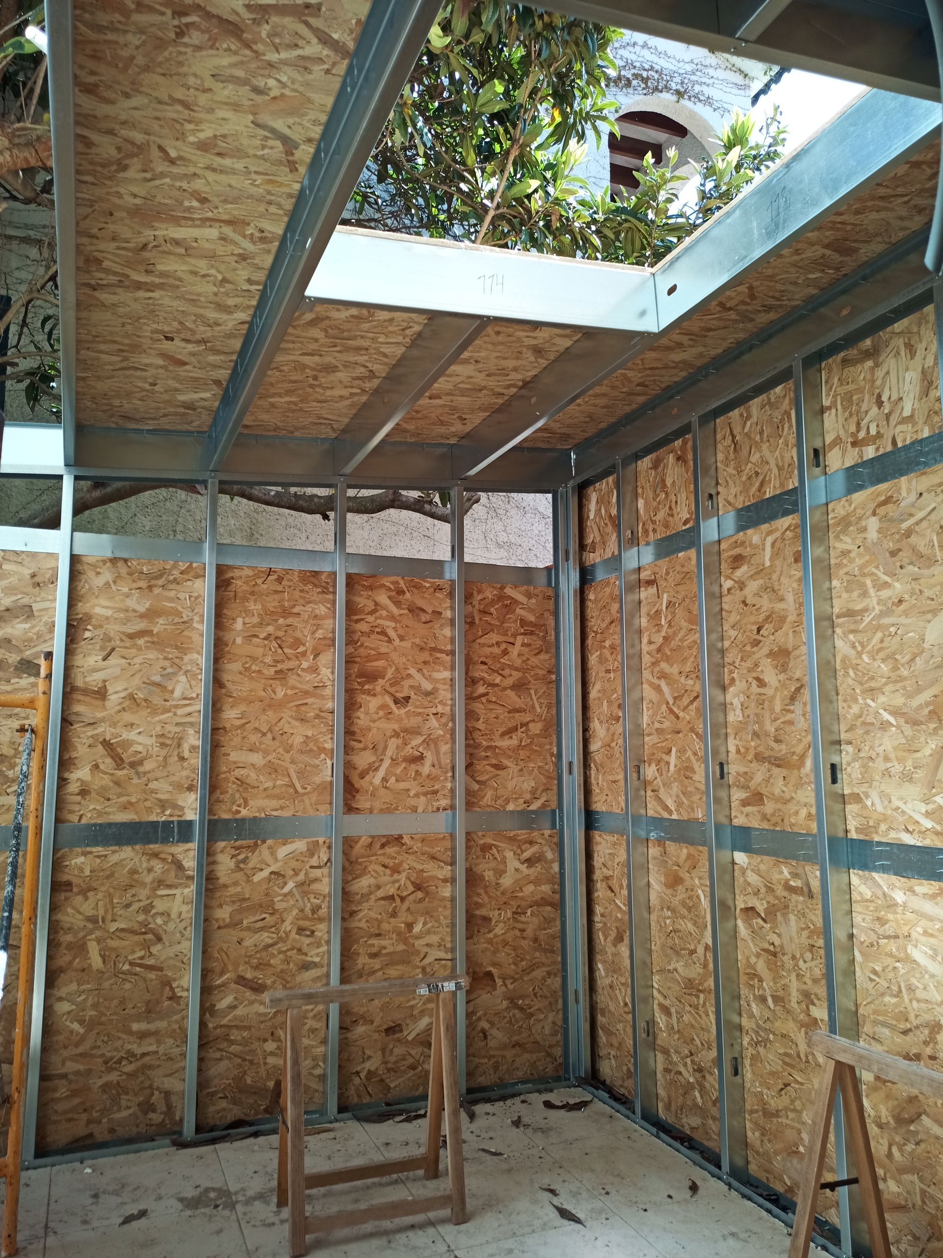 Interior de uma sala em construção, com estrutura metálica exposta e painéis OSB nas paredes e no teto.