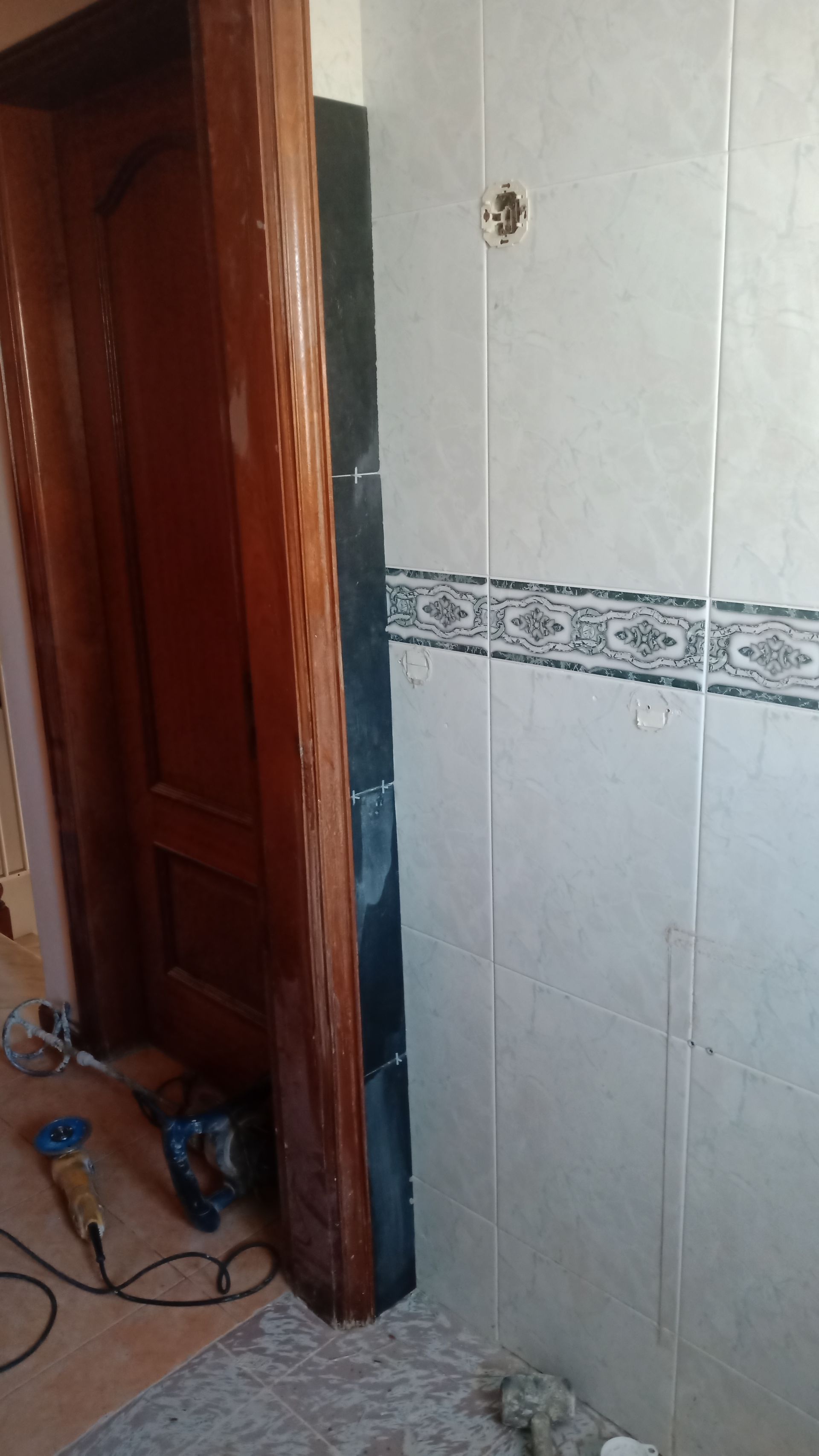 Reforma de banheiro com porta de madeira, parede revestida com azulejos e ferramentas no chão.