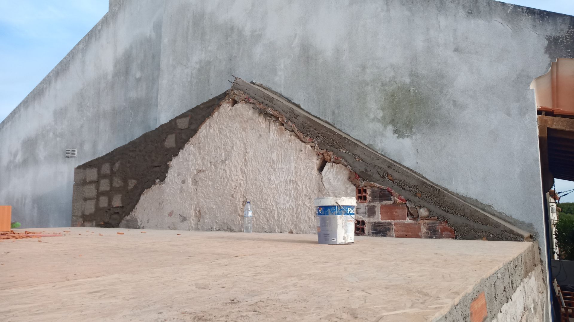 Construção no telhado: estrutura de tijolos e concreto; balde de tinta sobre o telhado plano próximo a uma parede inacabada.