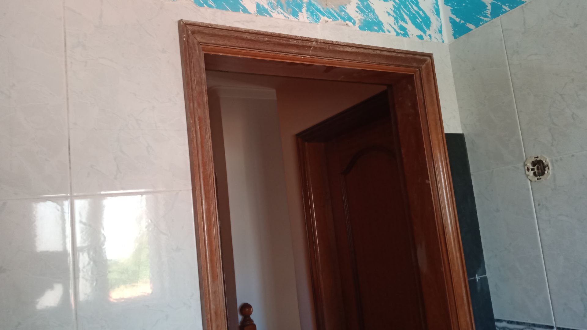 Batente de porta de madeira contra parede de azulejos; vista interior.