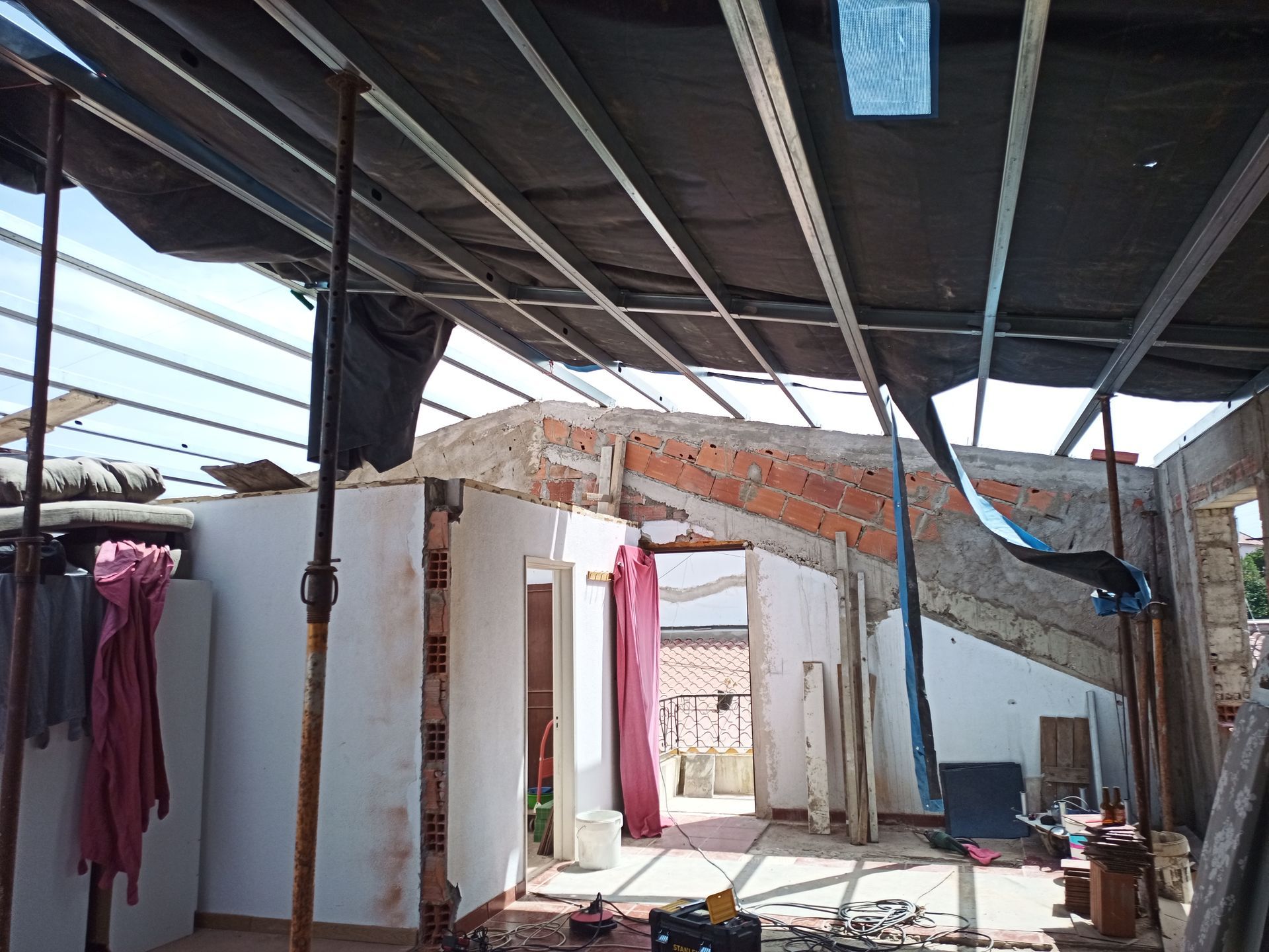 Interior de um edifício em construção. Tijolos aparentes, estrutura metálica e parte do telhado.