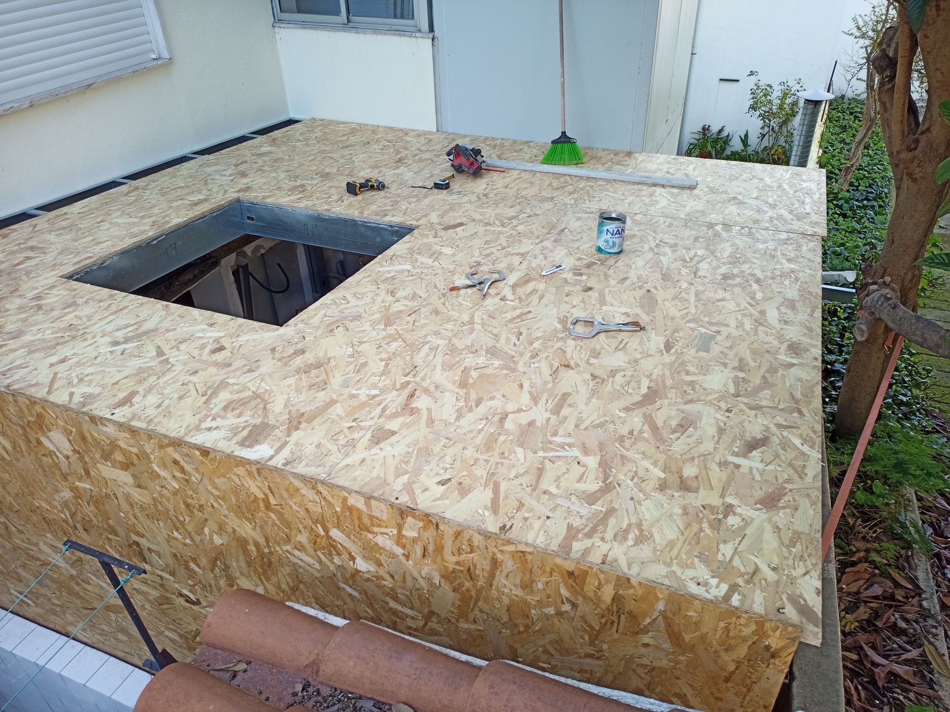 Estrutura de madeira revestida com OSB e com abertura quadrada. Ferramentas espalhadas sobre a superfície superior, em ambiente externo.