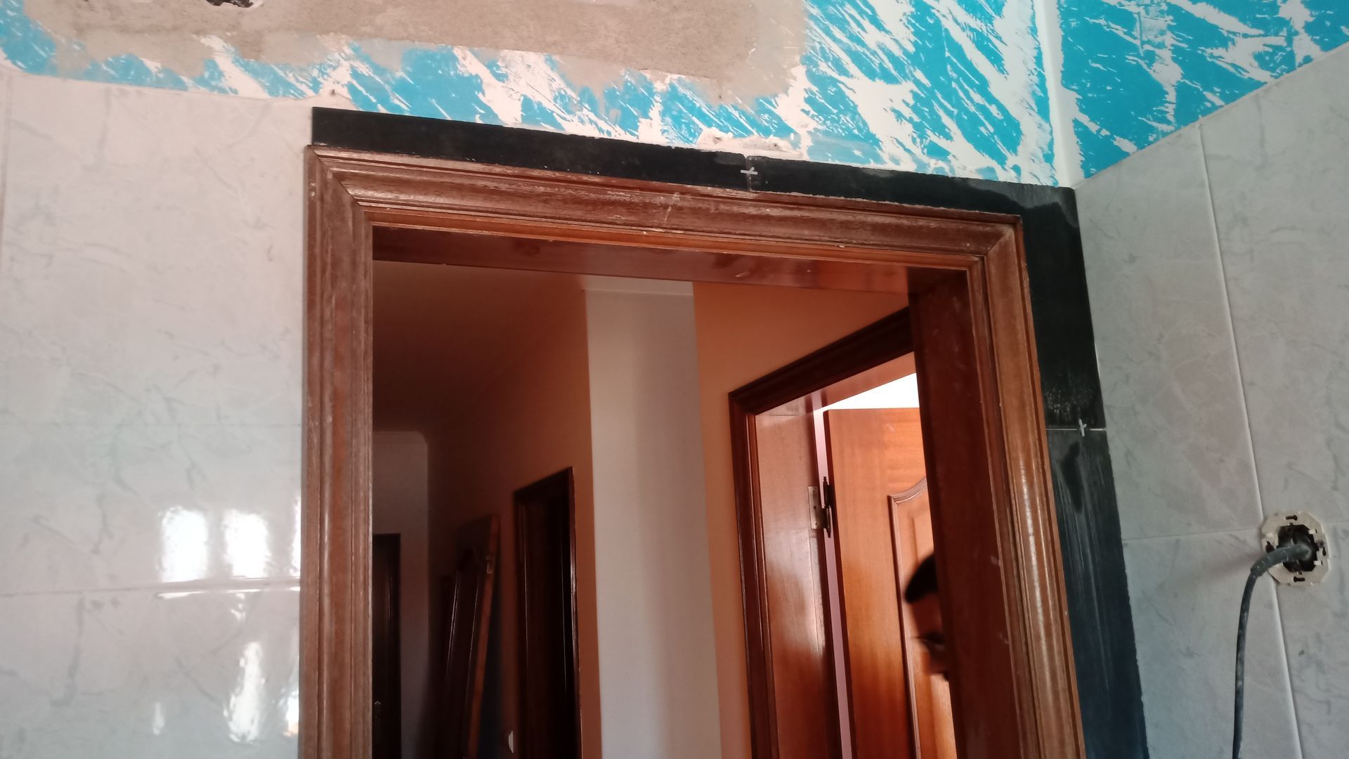 Porta com moldura decorativa de madeira e borda de pedra escura. Corredor interno visível.