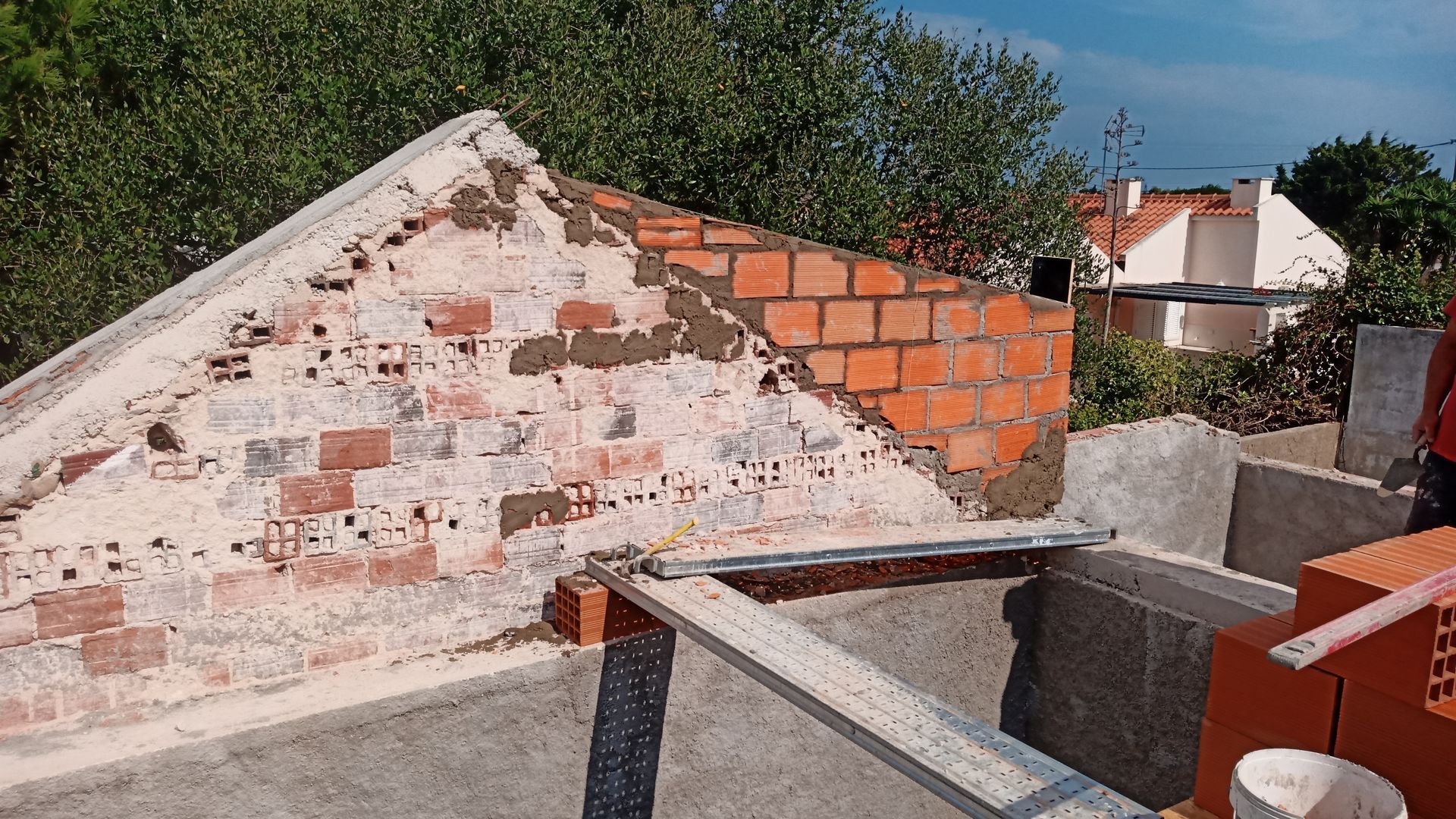 Construção em tijolos em um telhado, parcialmente concluída. Tijolos vermelhos, argamassa e concreto cinza.