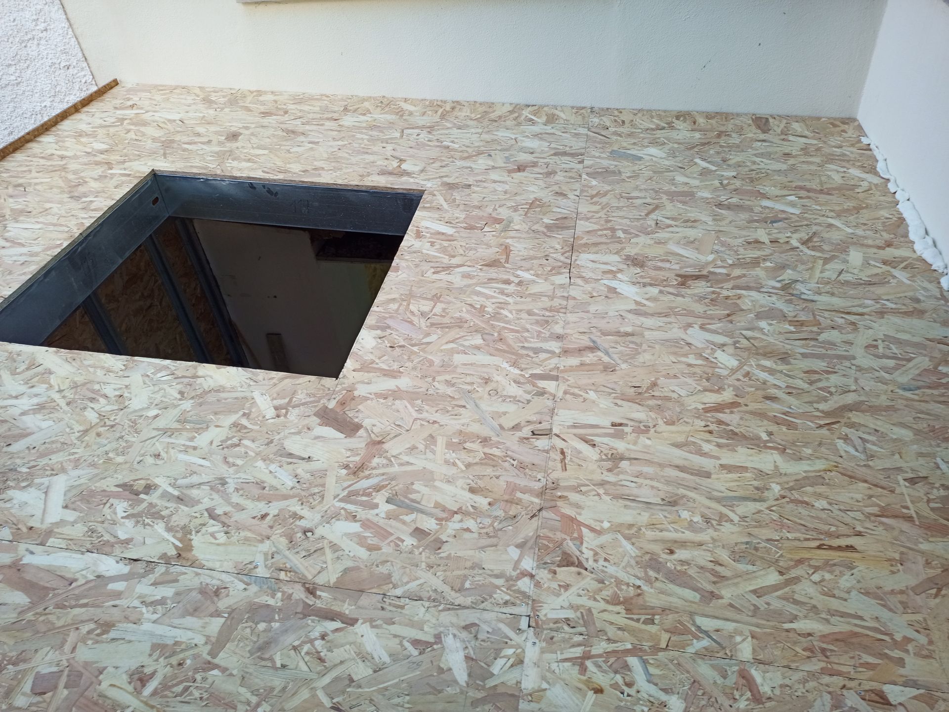 Piso de OSB com uma abertura quadrada que revela um espaço escuro abaixo.