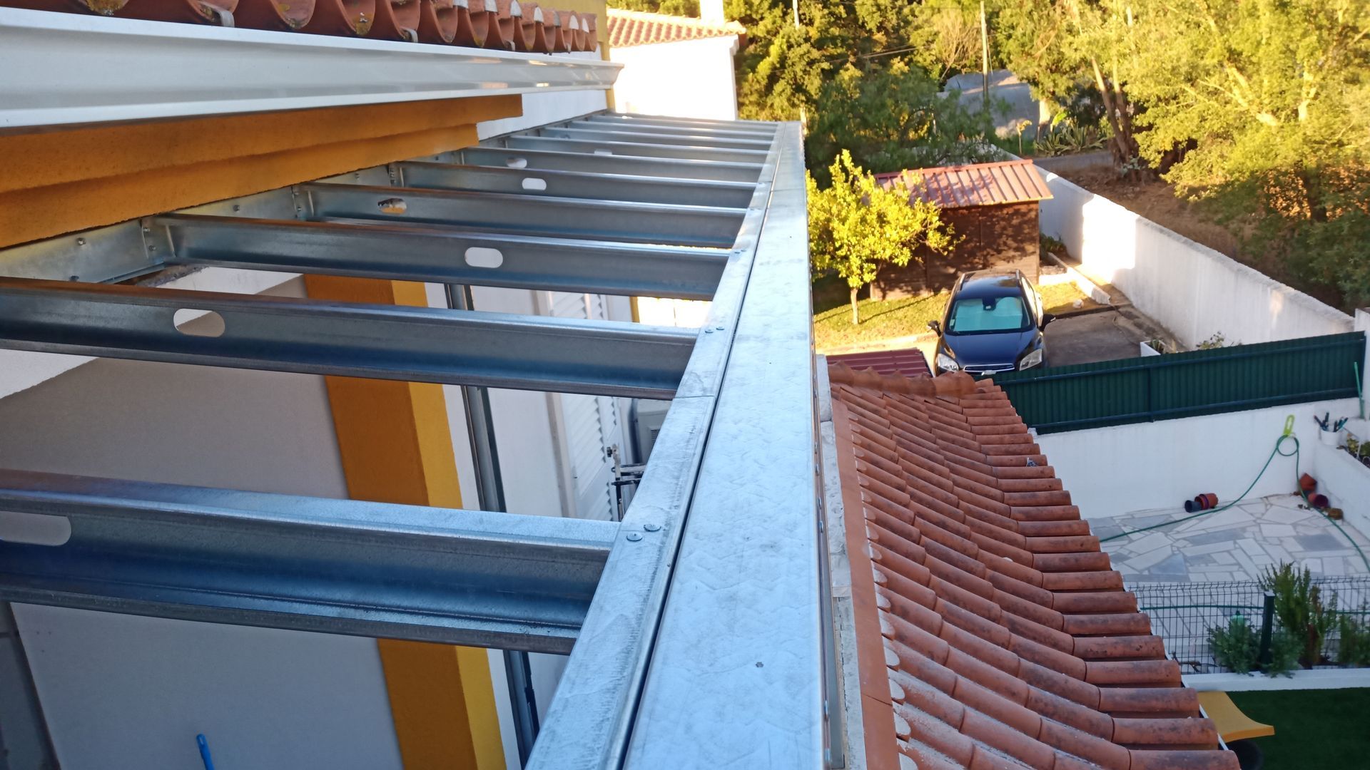 Estrutura metálica no telhado com telhas vermelhas e detalhes em amarelo.
