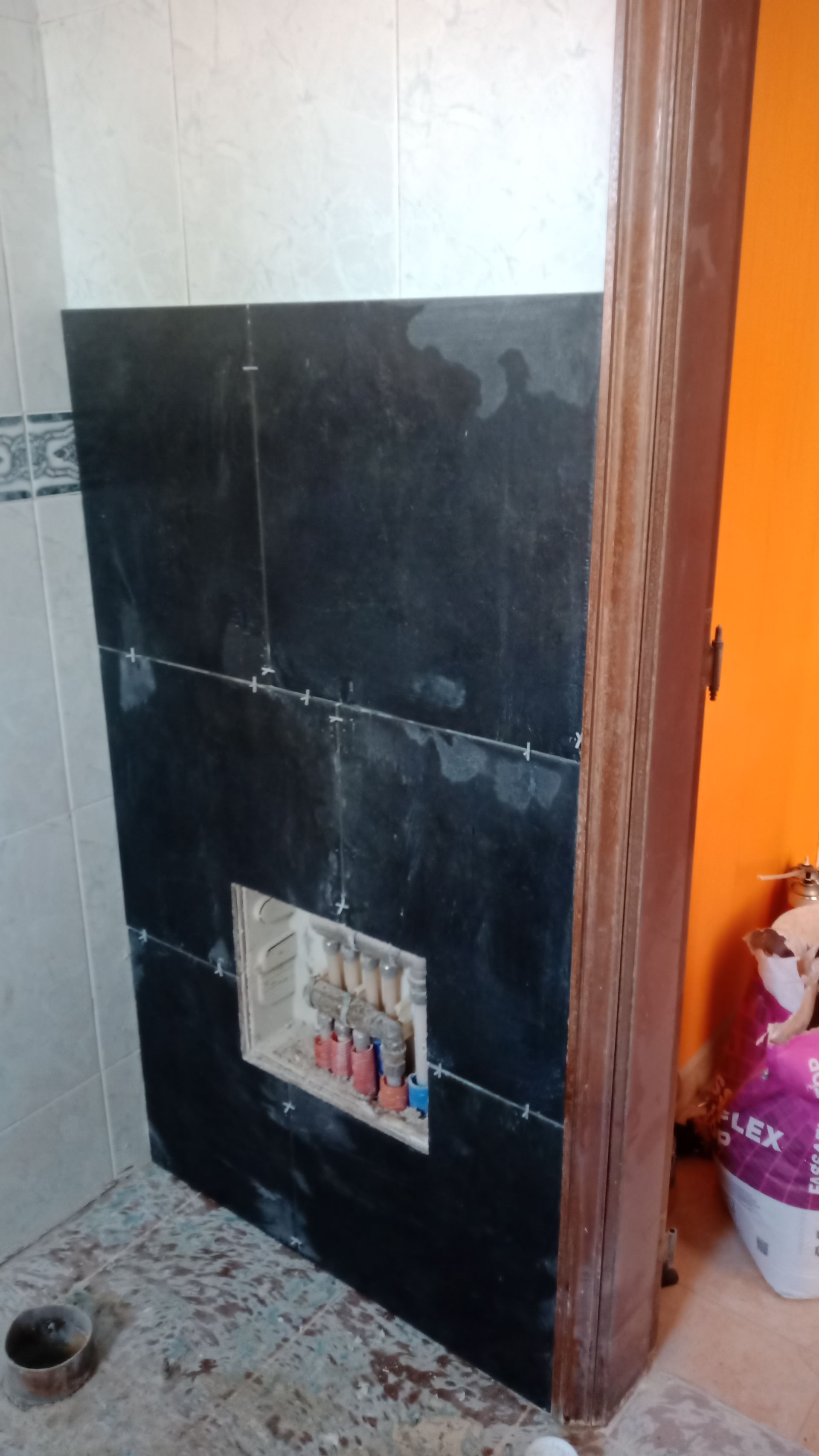 Parede do banheiro com azulejos escuros instalados, incluindo uma abertura para acessórios de encanamento.