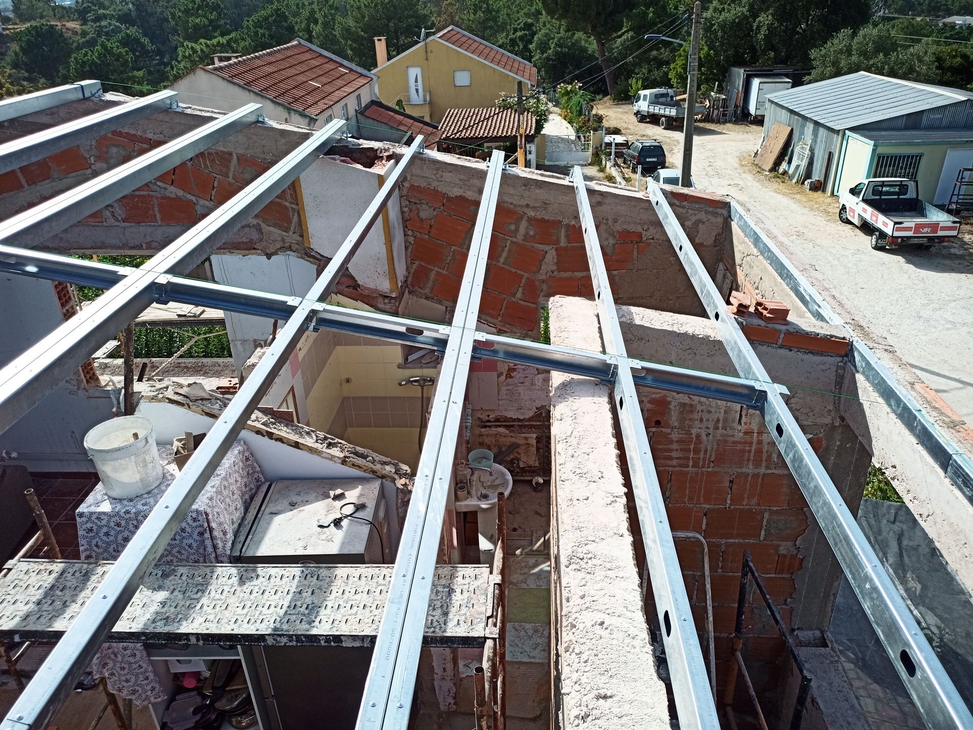 Instalação de estrutura metálica no telhado de um edifício de tijolos parcialmente demolido, vista exterior.