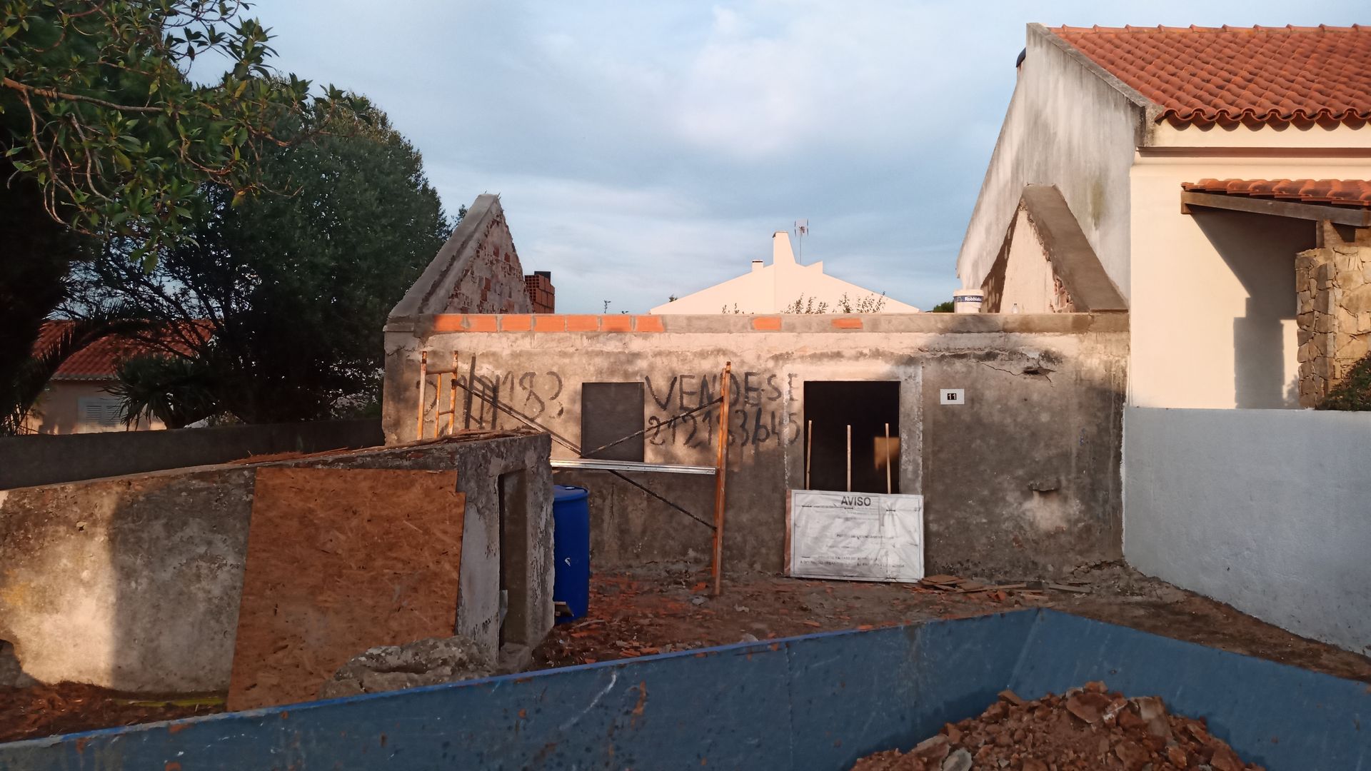 Prédio antigo e desgastado, com paredes parcialmente demolidas e telhado de telhas vermelhas, sob um céu nublado.