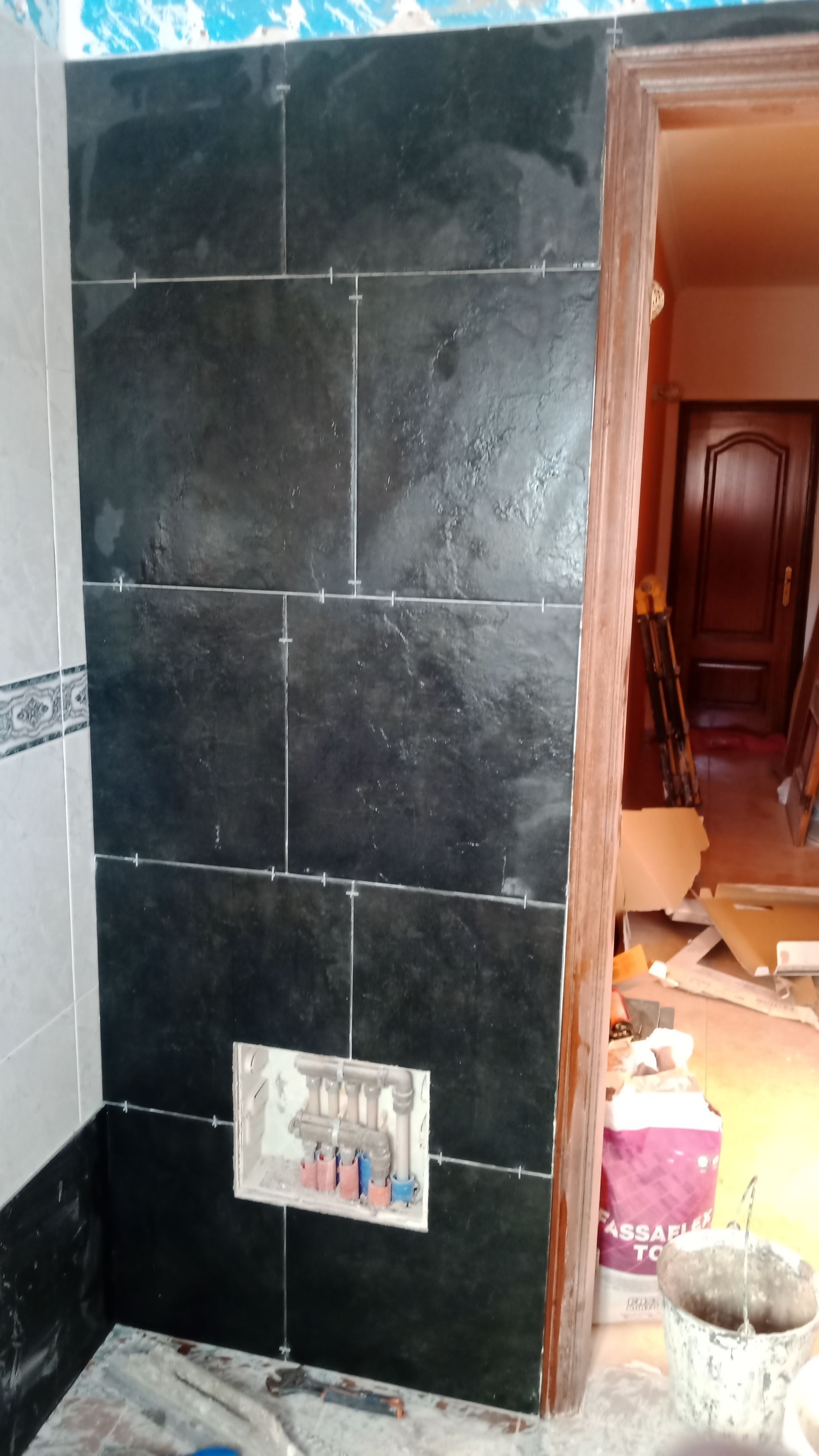 Parede revestida com azulejos pretos e nicho embutido, ao lado de uma porta.