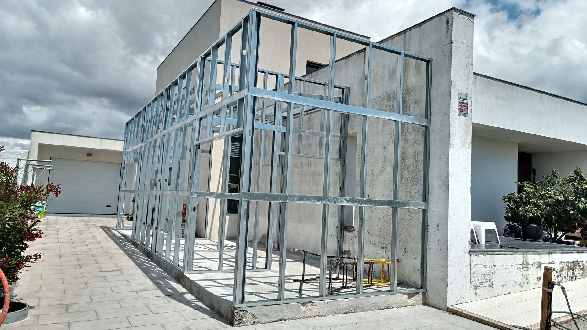 Estrutura metálica para um anexo externo construído em um prédio branco sob um céu nublado.