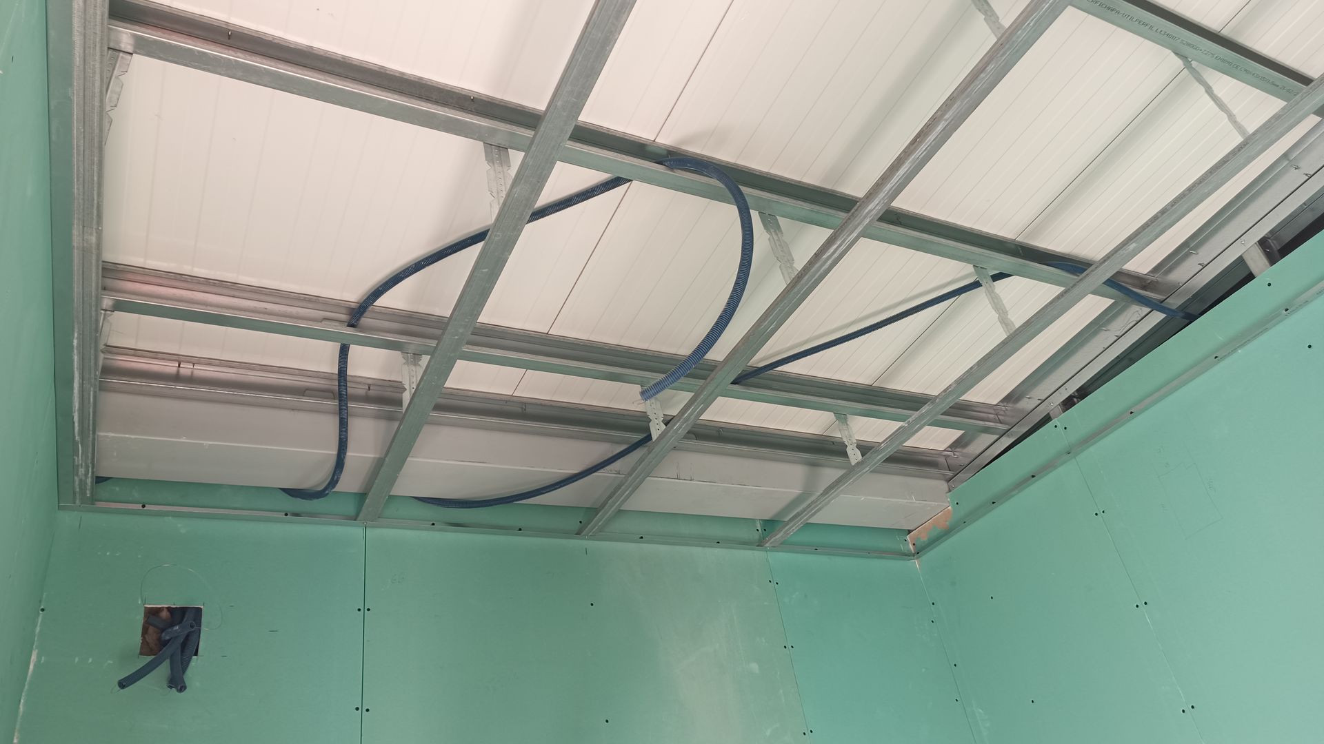 Forro de estrutura metálica em construção, com conduítes elétricos azuis e paredes verdes.