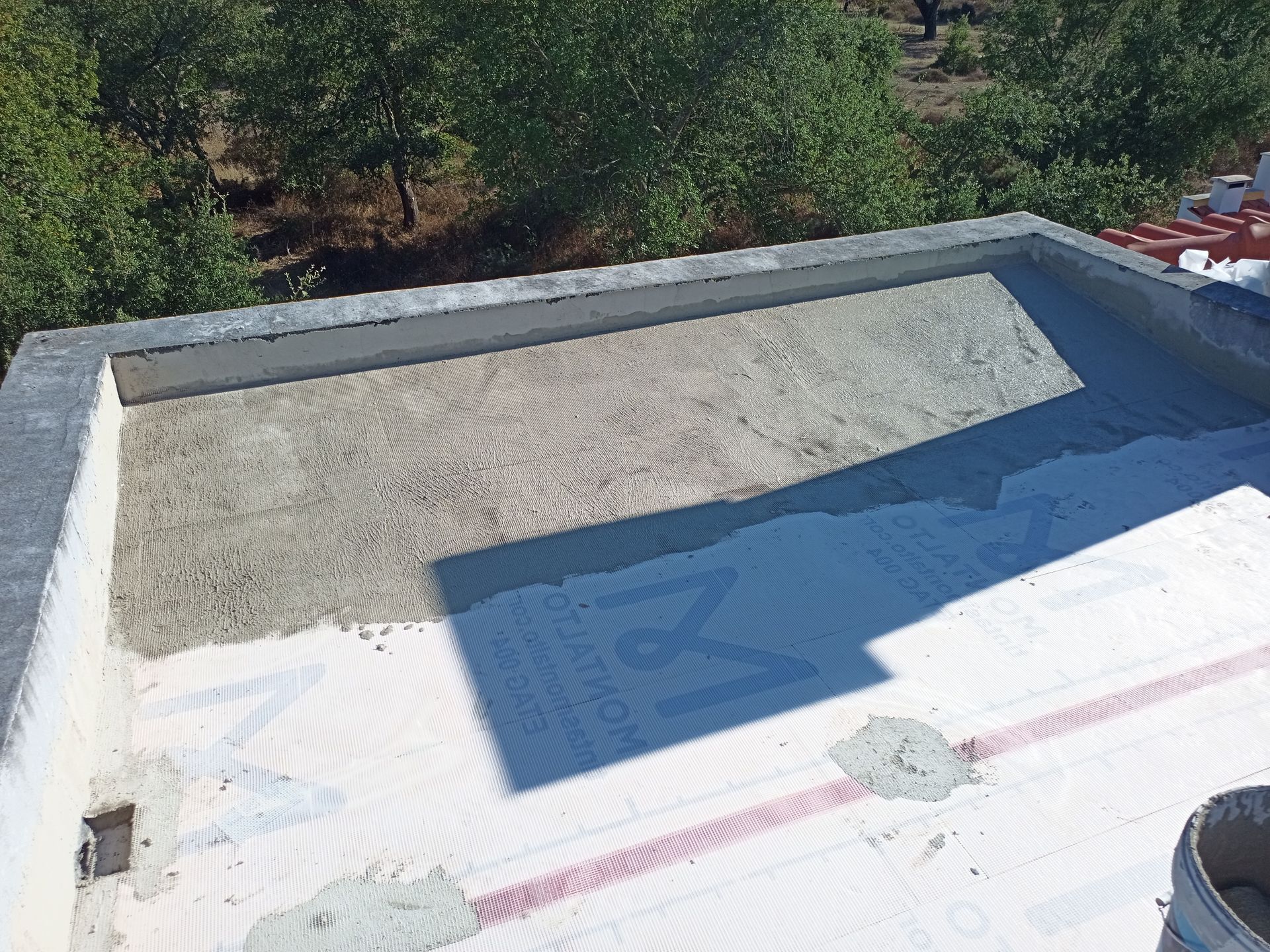 Telhado com concreto cinza claro e uma seção coberta com tela branca. Uma obra está em andamento na área externa.