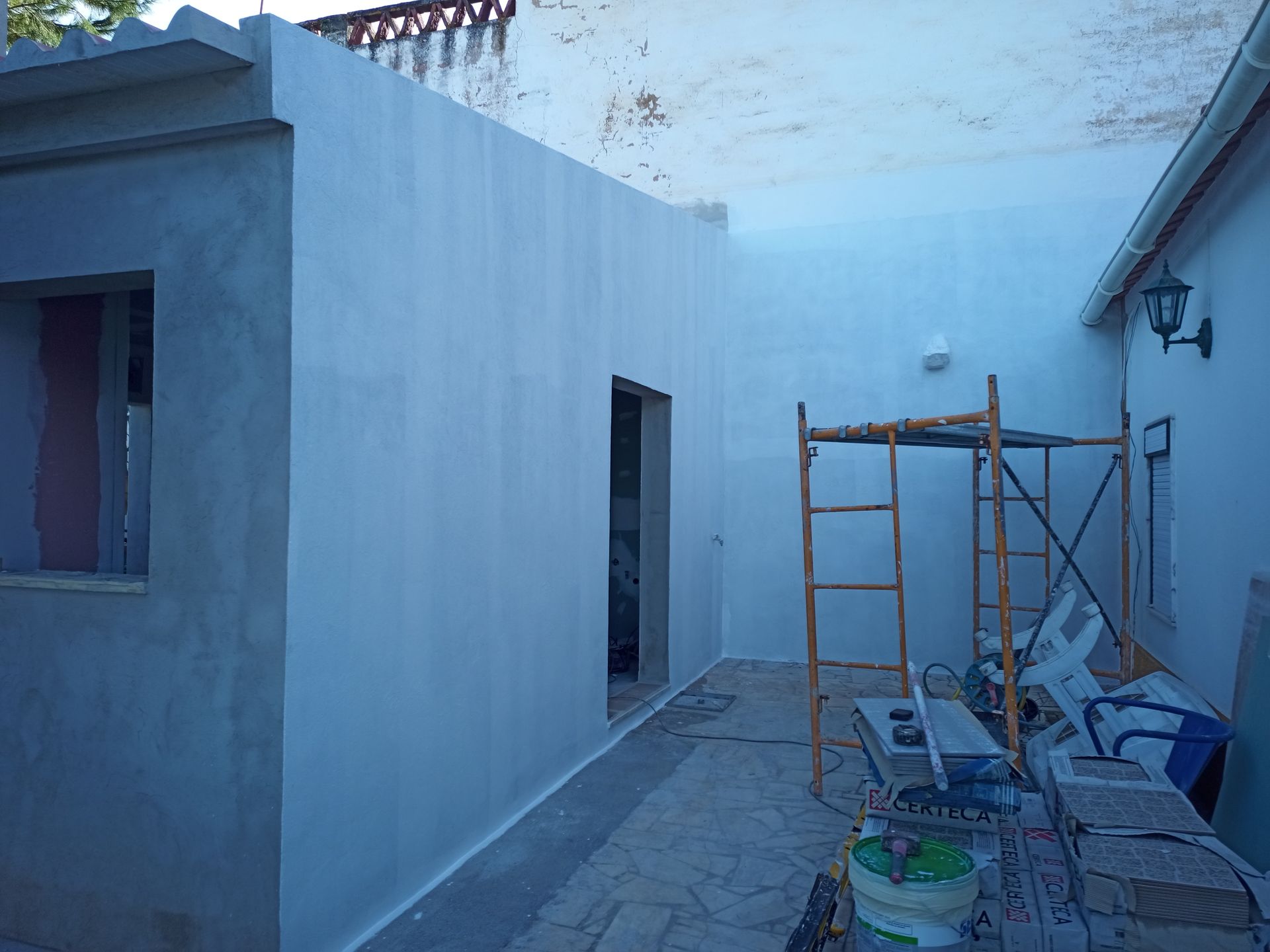 Exterior de um prédio em construção, paredes brancas, porta, janela, andaime, ferramentas de construção.