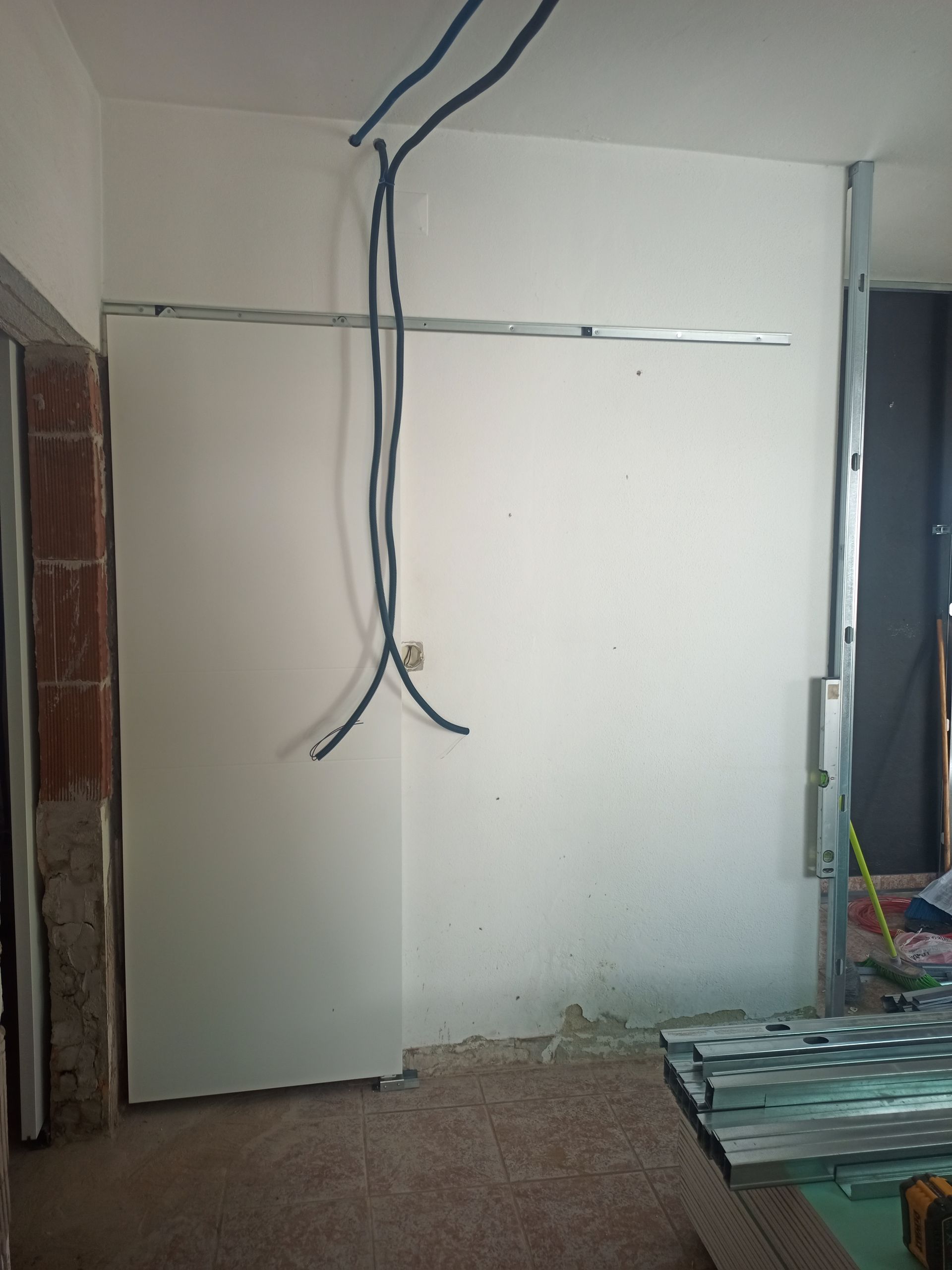 Instalação de drywall em andamento. Parede branca com estrutura metálica exposta, fiação elétrica e materiais de construção.