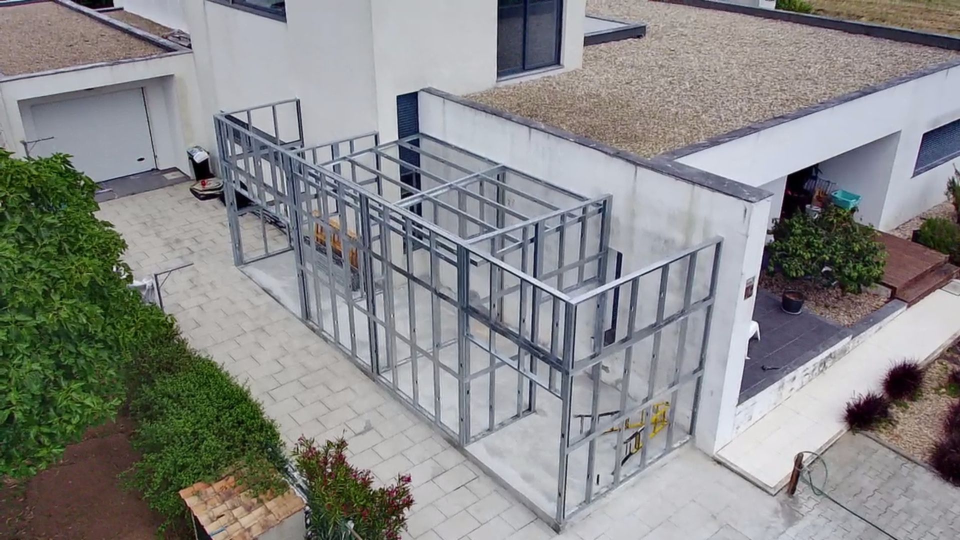 Estrutura metálica para uma construção externa anexa a um edifício branco. Construção térrea com laterais abertas.