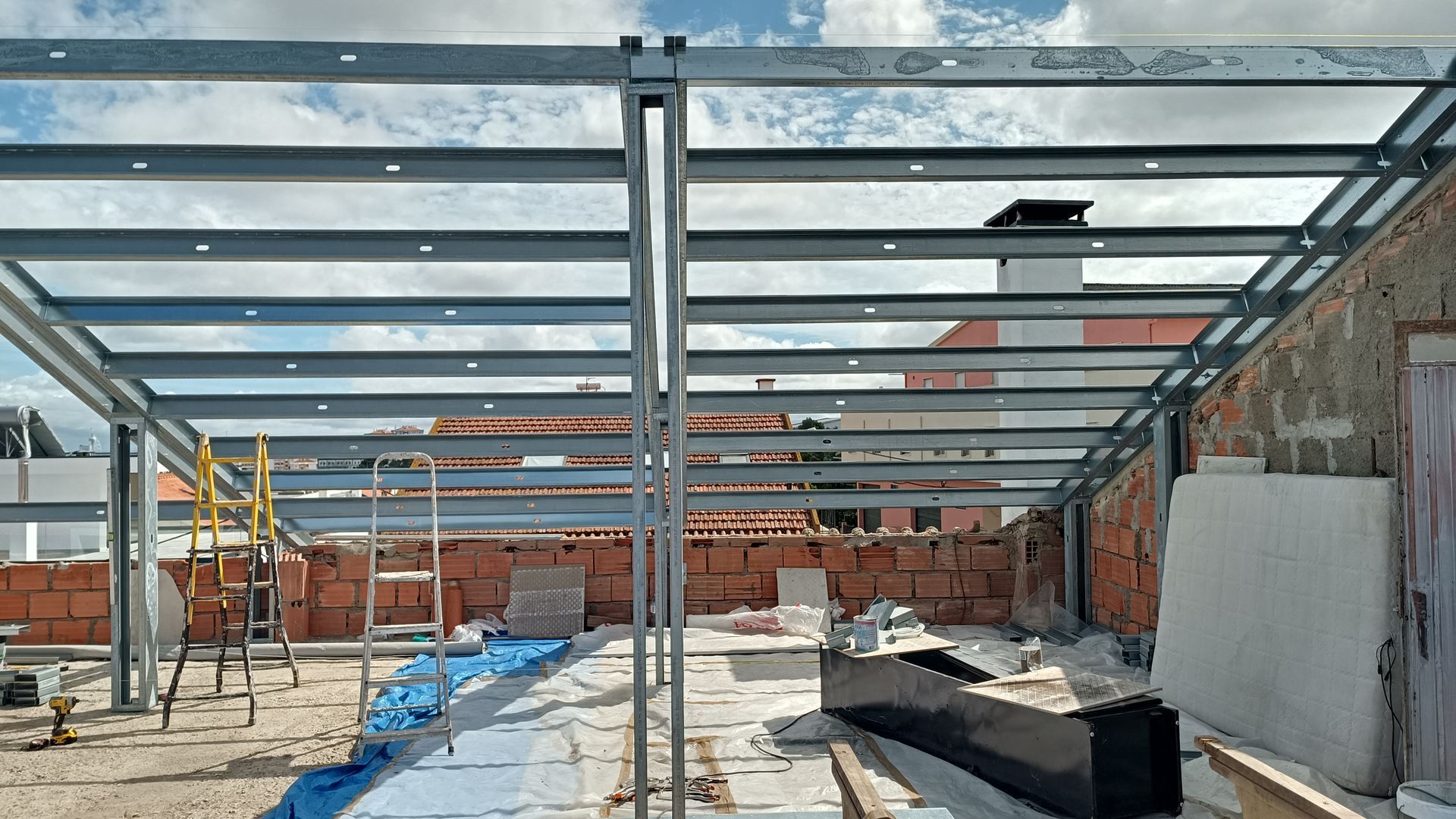 Cobertura com estrutura de aço em construção em um telhado com paredes de tijolos, lona azul e escadas.